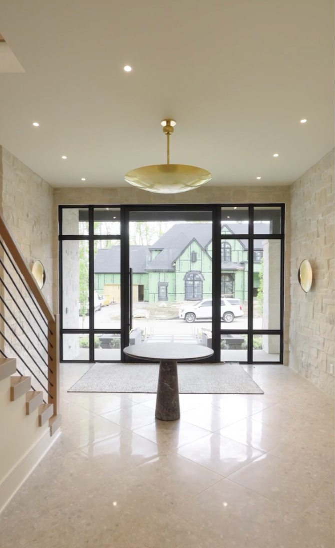 Modern entryway with glass front door, stone walls, and round table with stone base.