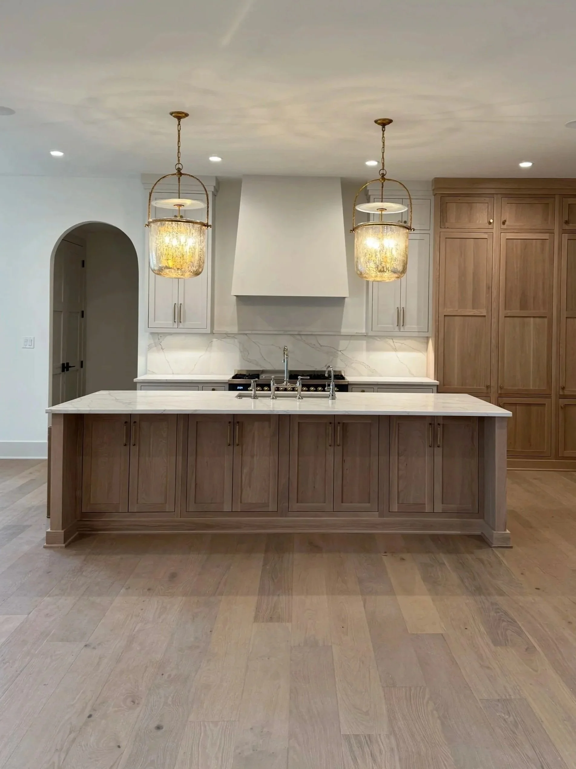 Modern kitchen with pendant lights, wooden cabinets, marble countertops, and a kitchen island.