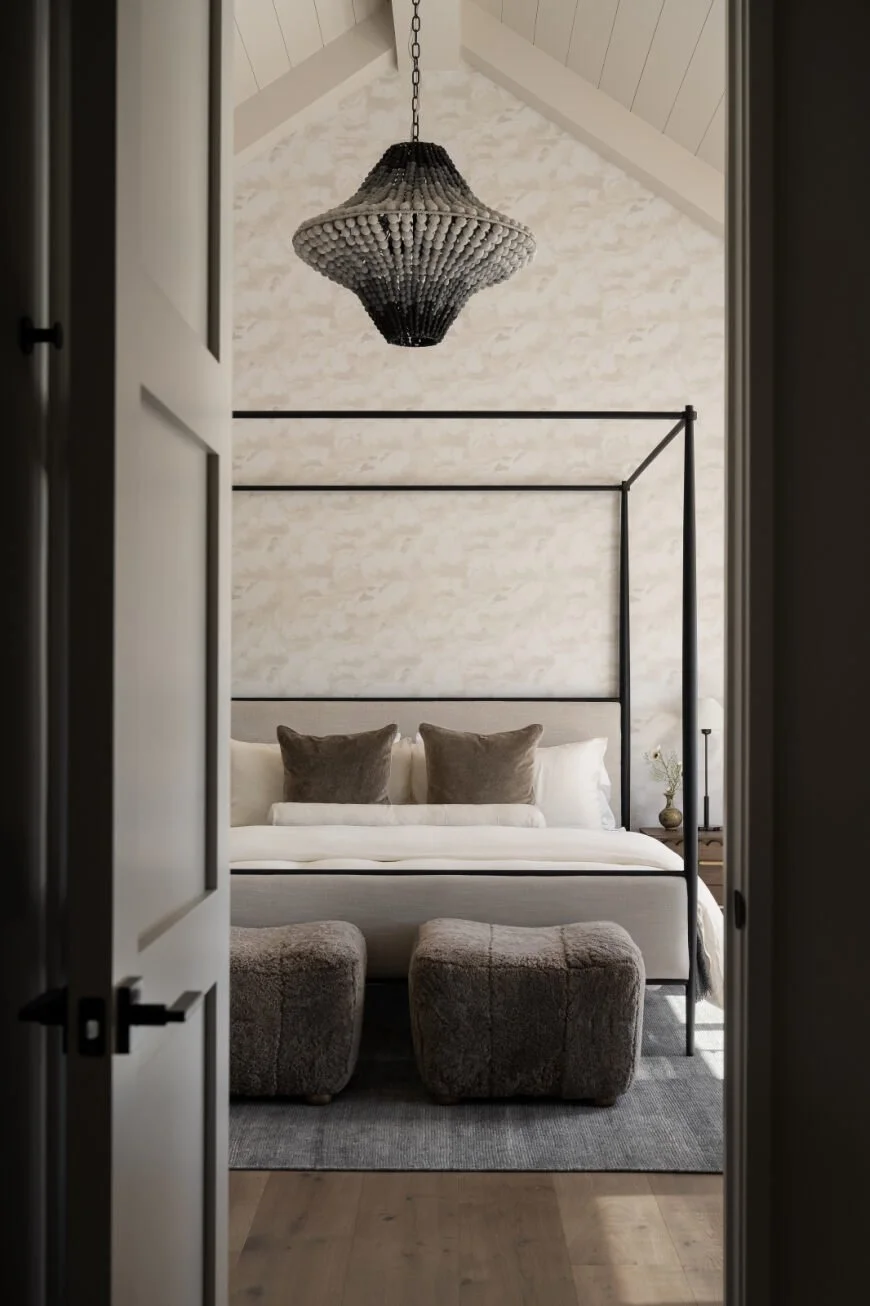 Textured wallpaper, vaulted ceiling detailing, and a sculptural statement chandelier frame this layered bedroom retreat.