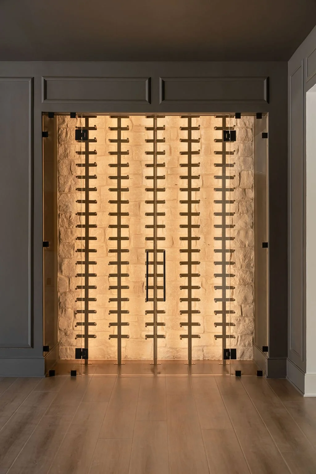 A modern wine cellar with a glass door, illuminated brick wall background, and wooden wine racks.