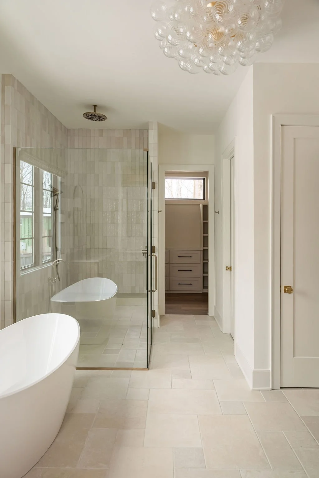 Modern bathroom with a freestanding bathtub, glass shower enclosure, window, and a walk-in closet with built-in shelves and drawers.