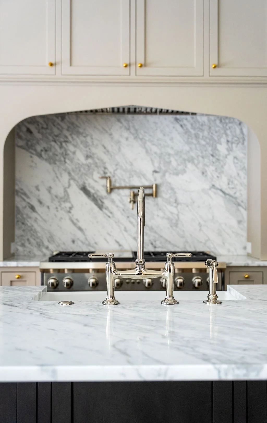 Modern kitchen with marble countertop and backsplash, stainless steel faucet, and white cabinets with gold knobs.