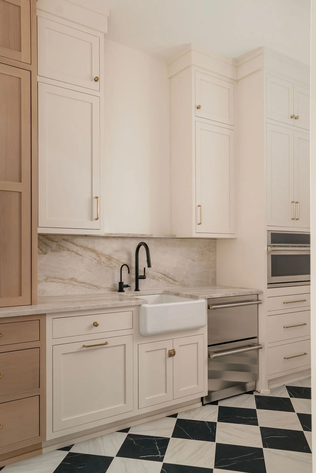 Kitchen with white cabinets, marble countertops, black and white checkered tile flooring, and a farmhouse sink with black fixtures.