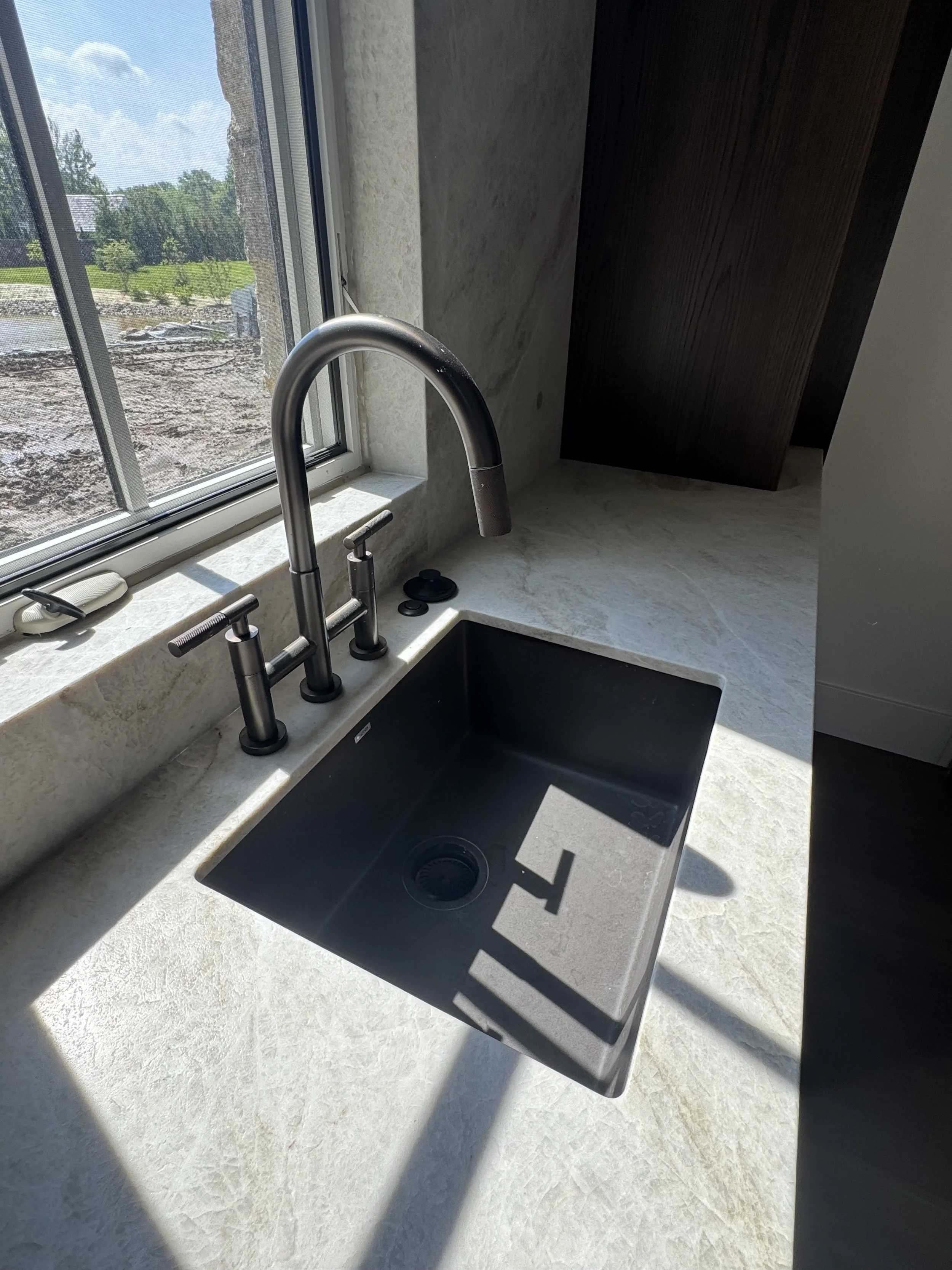Kitchen sink with black basin, silver faucet, and window with view of an outdoor landscape.