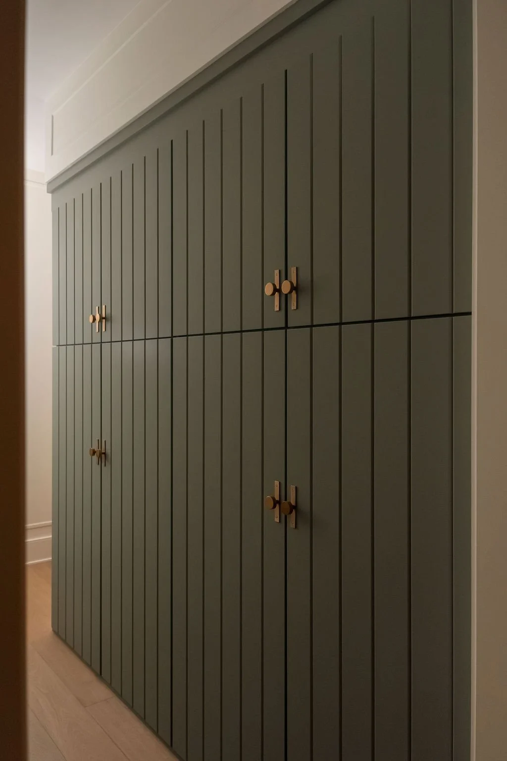 A set of green, vertically paneled cabinet doors with round wood knobs in a hallway or room.