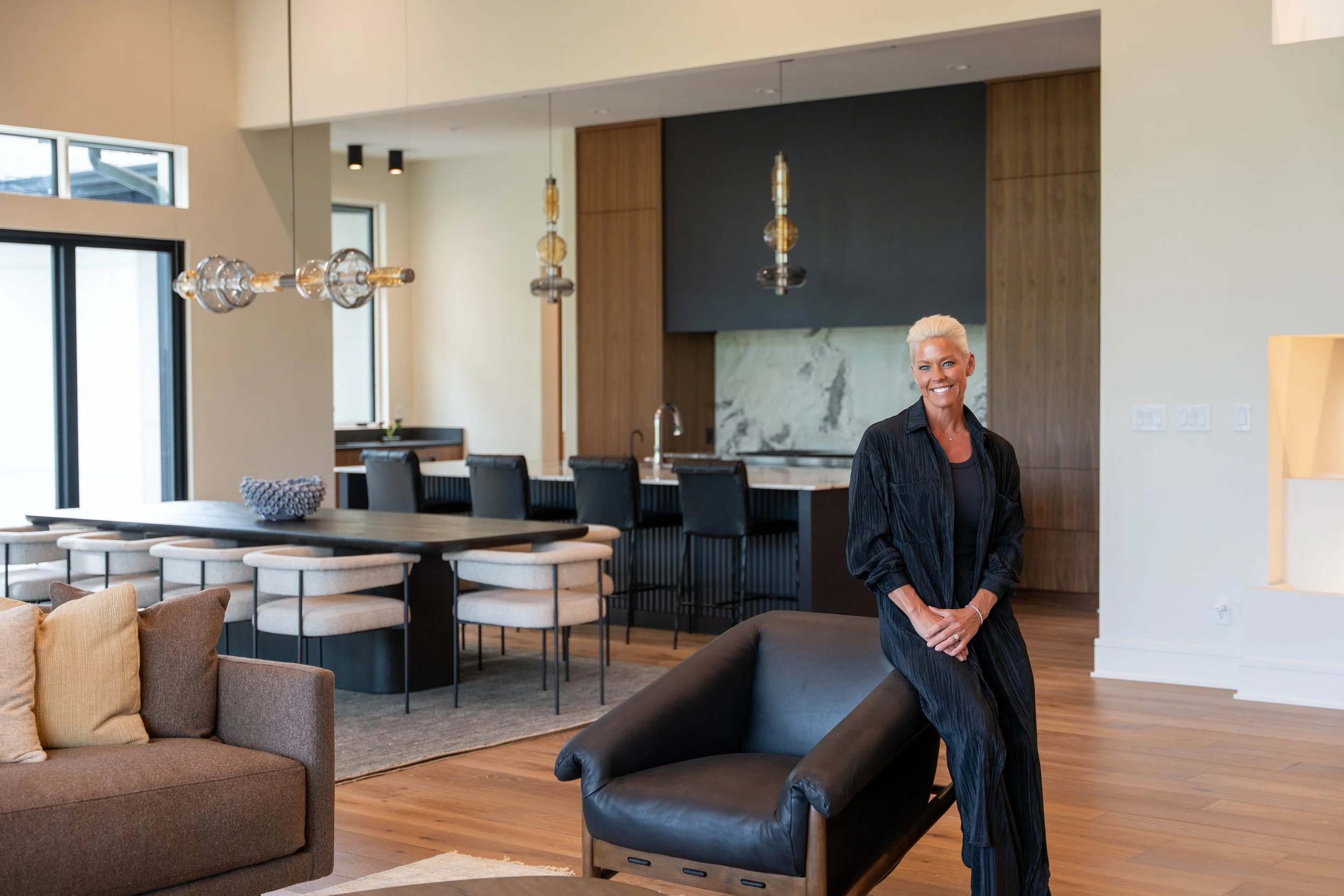 Modern open-concept living room and kitchen space featuring contemporary pendant lights, wood flooring, and natural light.