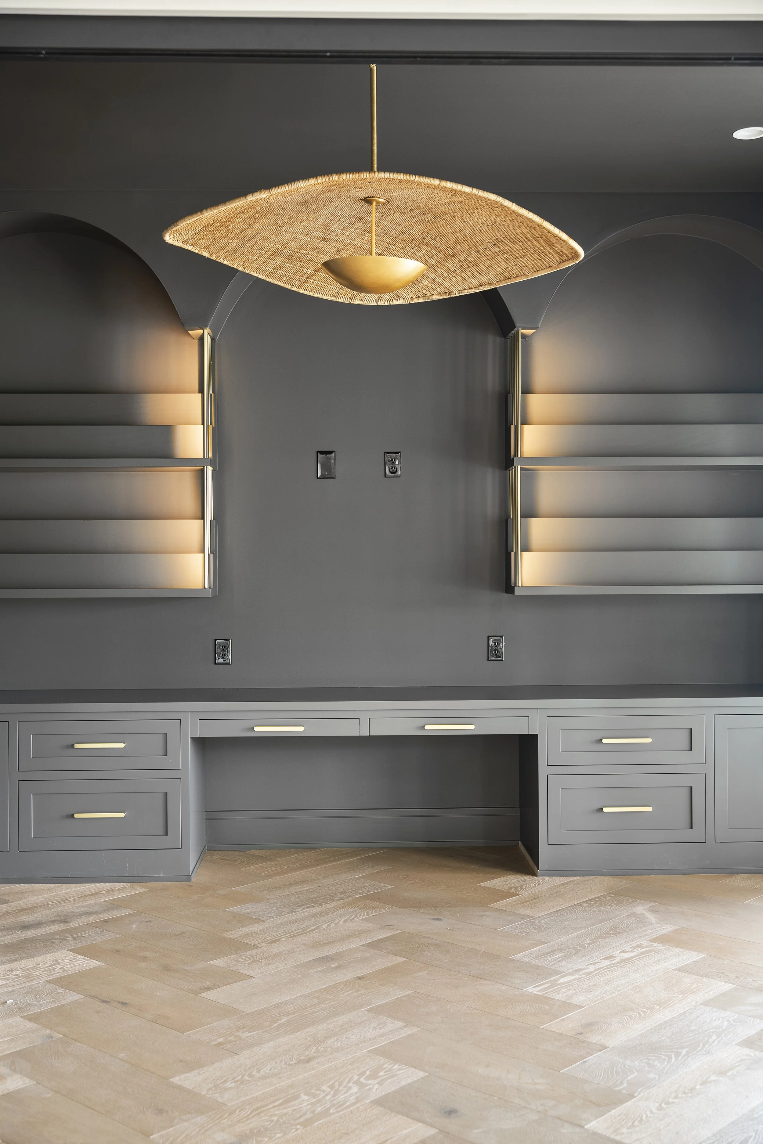 Modern kitchen with gray cabinetry, light hardwood flooring, and a contemporary ceiling light fixture with a woven shade and brass accents.