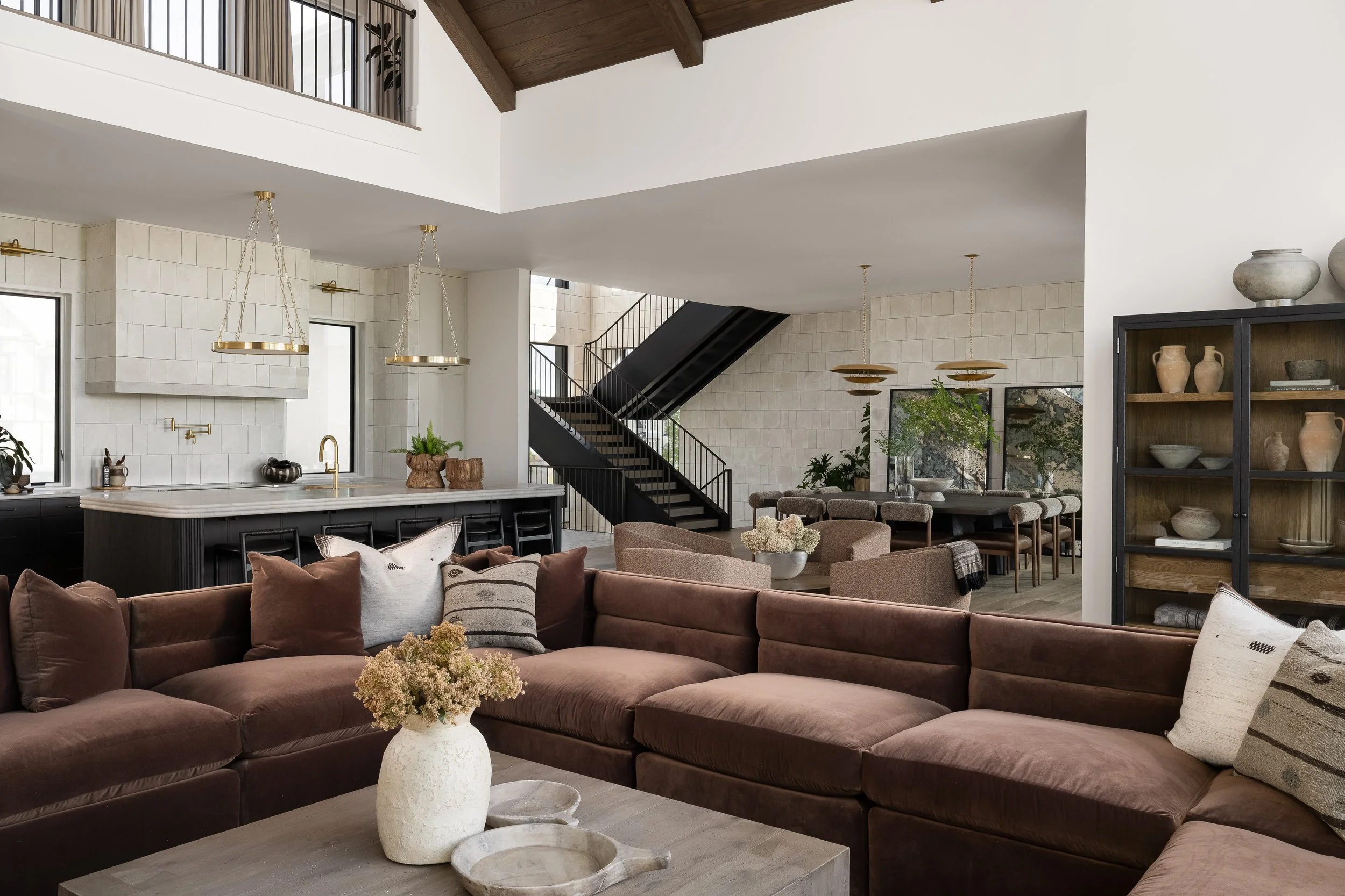 Stone wall detailing, dark wood ceiling beams, and mixed natural finishes carry throughout this modern organic open-concept space.