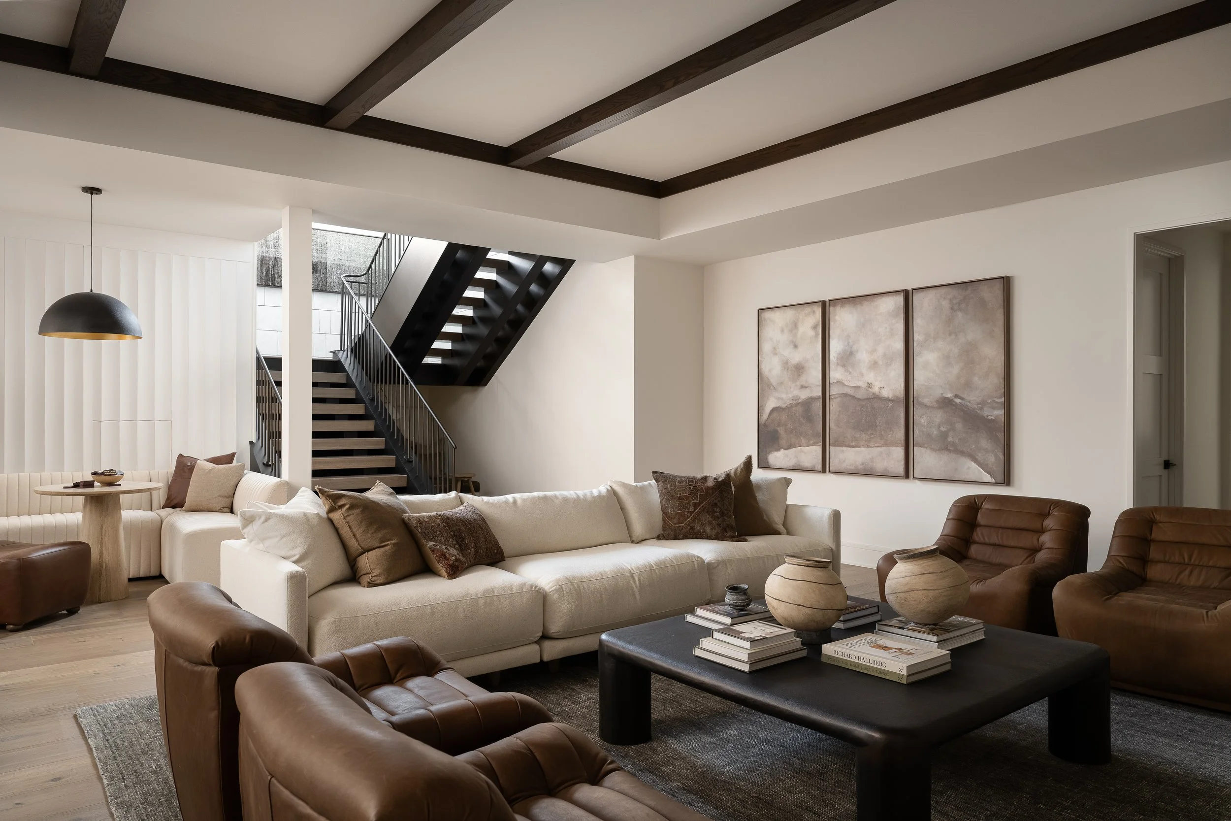 Dark ceiling beams, integrated wall paneling, and layered architectural lighting bring warmth and contrast to this lower level entertaining space.