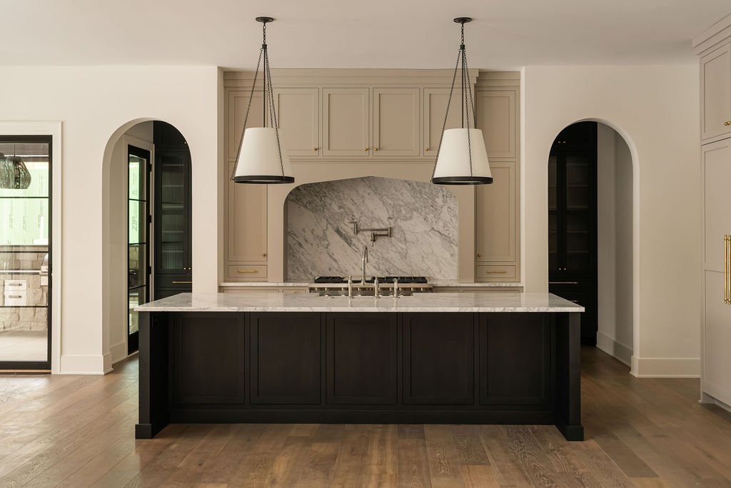 Modern kitchen with a black island, marble countertop, beige cabinetry, pendant lights, and a marble backsplash