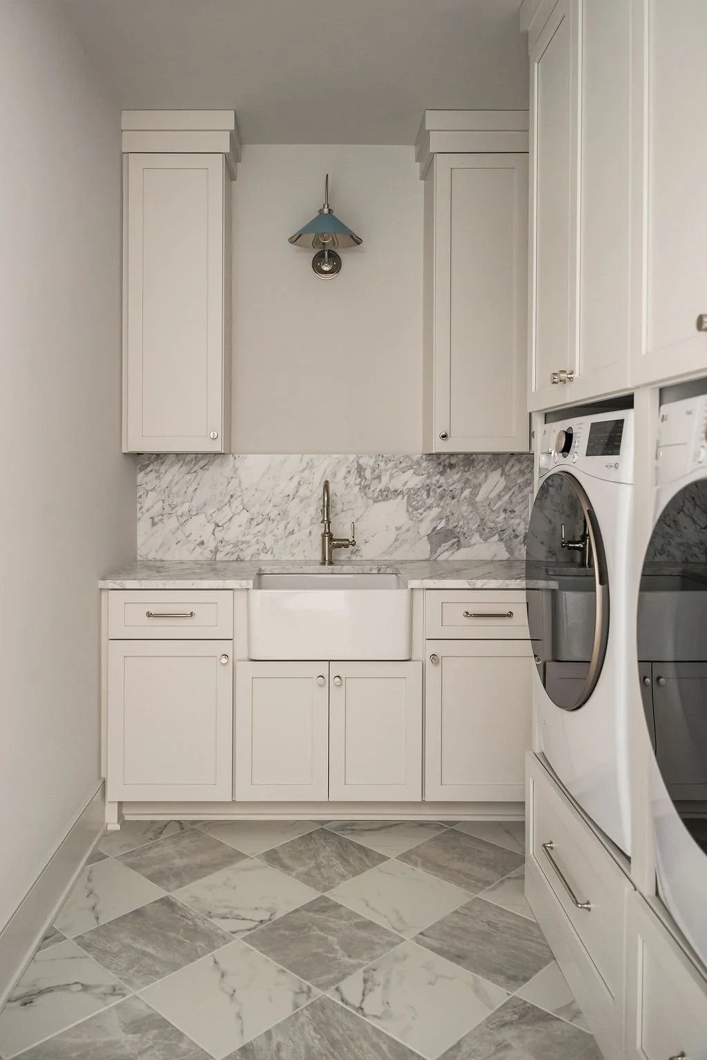 Laundry room with white cabinets, a marble backsplash, a farmhouse sink, a washing machine, and a dryer, with a blue lampshade hanging from the ceiling.