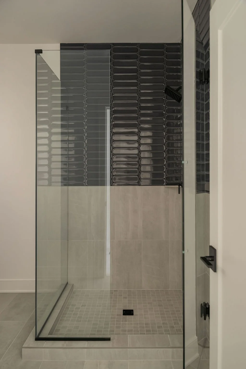 A modern glass shower with black tiles on the back wall and beige tiles on the floor.