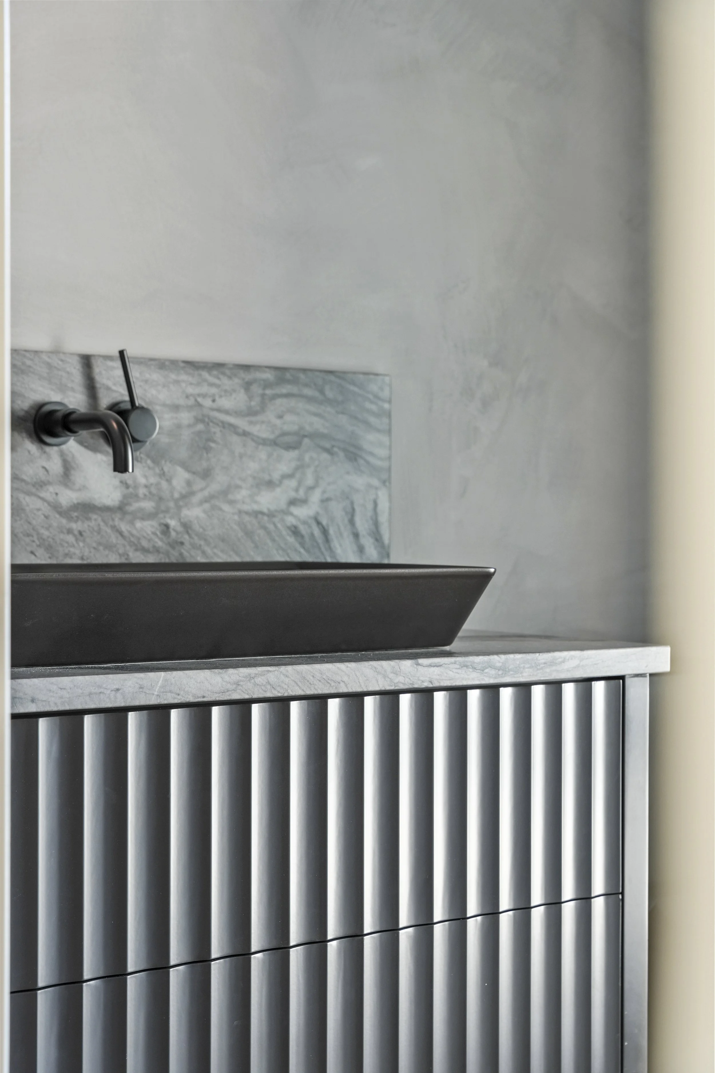 Close-up of a modern kitchen sink with a black faucet, marble countertop, and a decorative striped metal panel below.