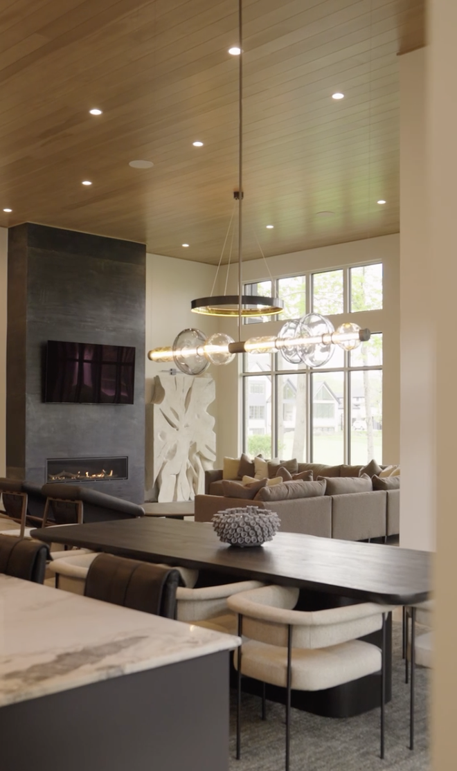 Modern living room with a wooden ceiling, large windows, and a fireplace, with a contemporary chandelier.