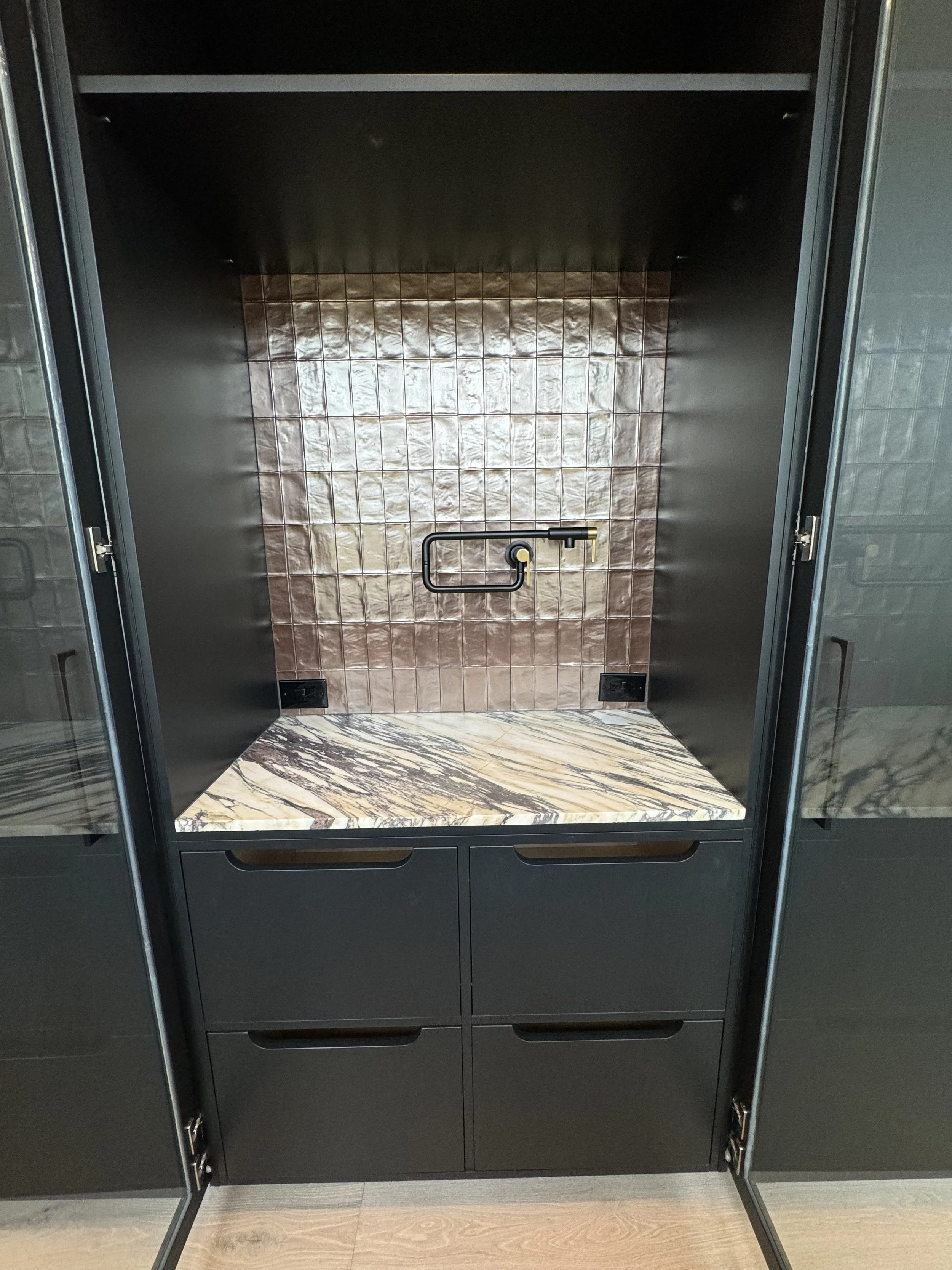 A modern display case with a marble top, a tiled backsplash, and black outer structure featuring drawers and doors.