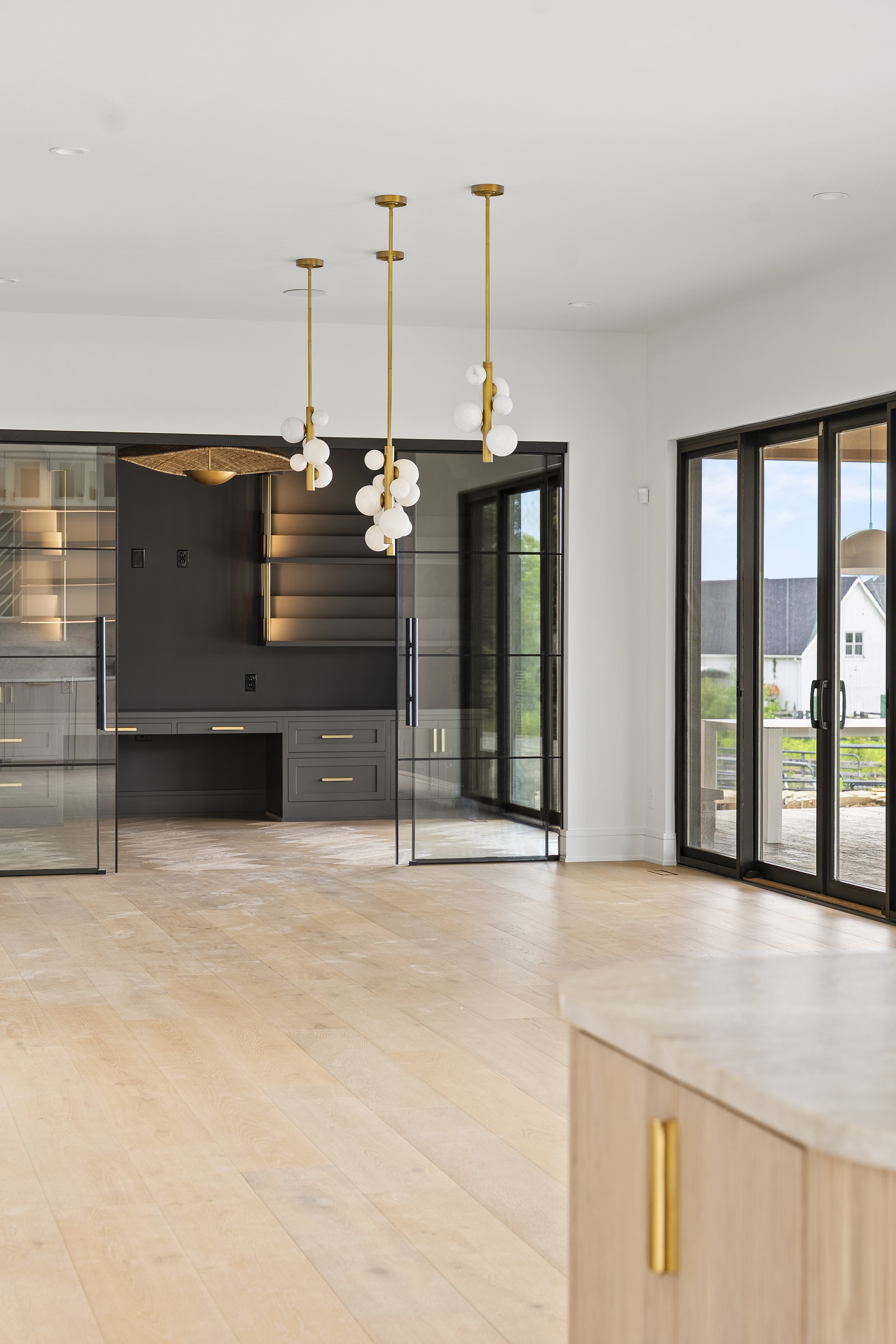 Modern interior living space with light wood floors, large sliding glass doors, and hanging pendant lights with white globes.