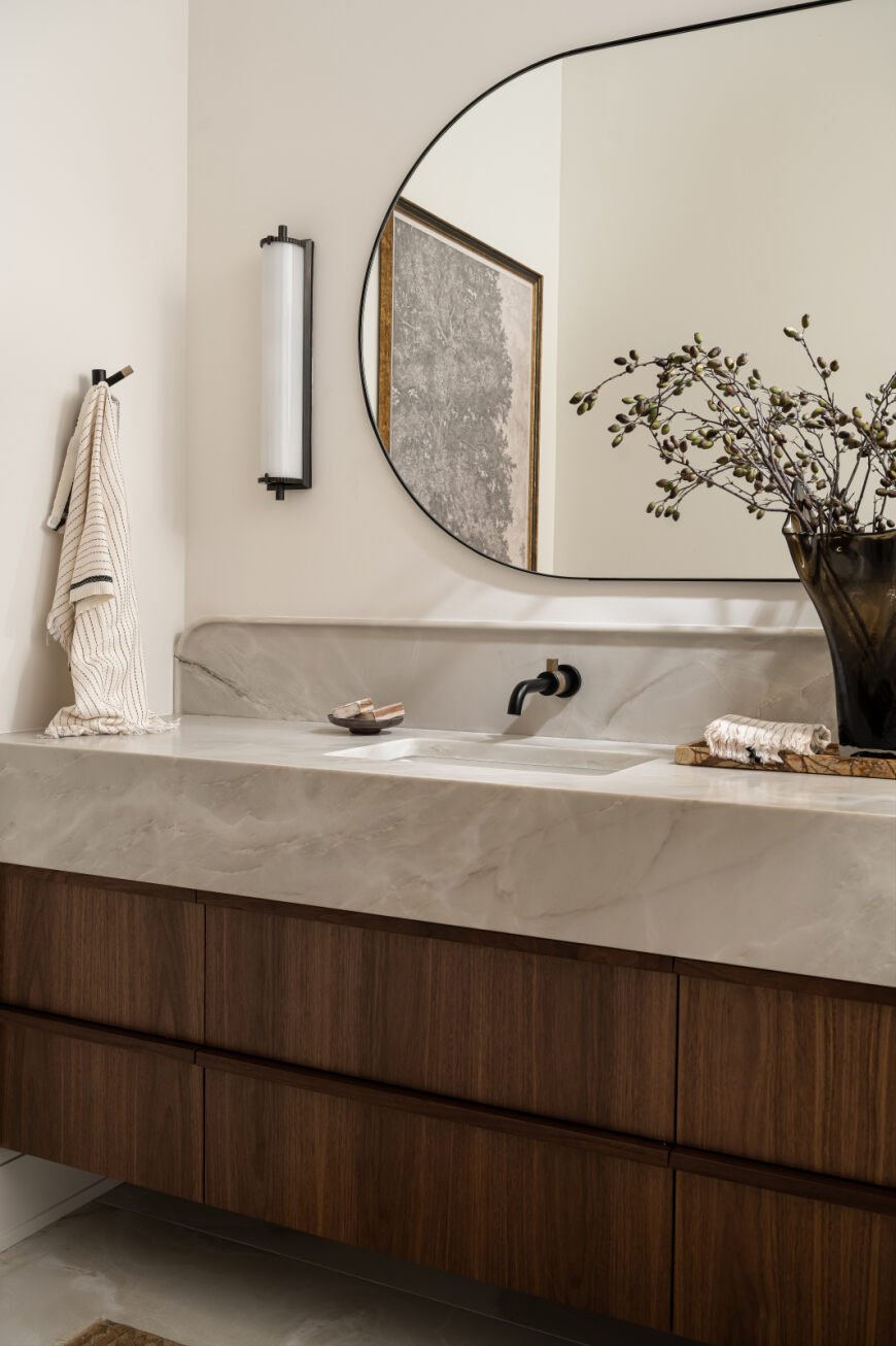 Floating walnut vanity paired with wall-mounted faucets and soft curved lines. 