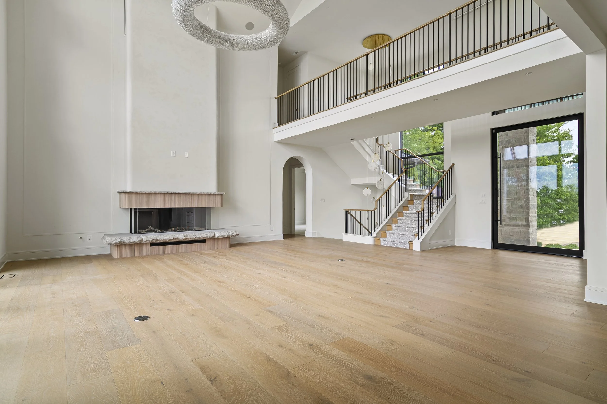 Modern living room with a light wooden floor, a fluted fireplace, and clean lined staircase.