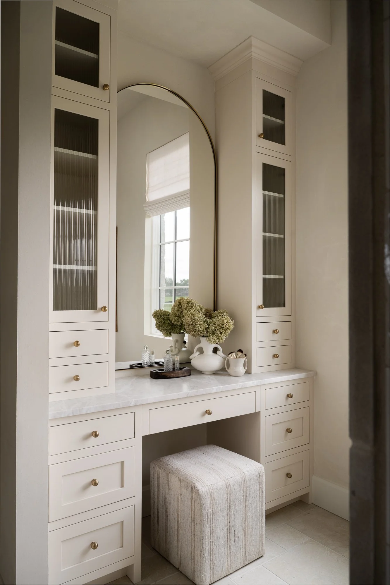 A luxurious warm white vanity with built-in cabinets, a marble countertop, and a large mirror.