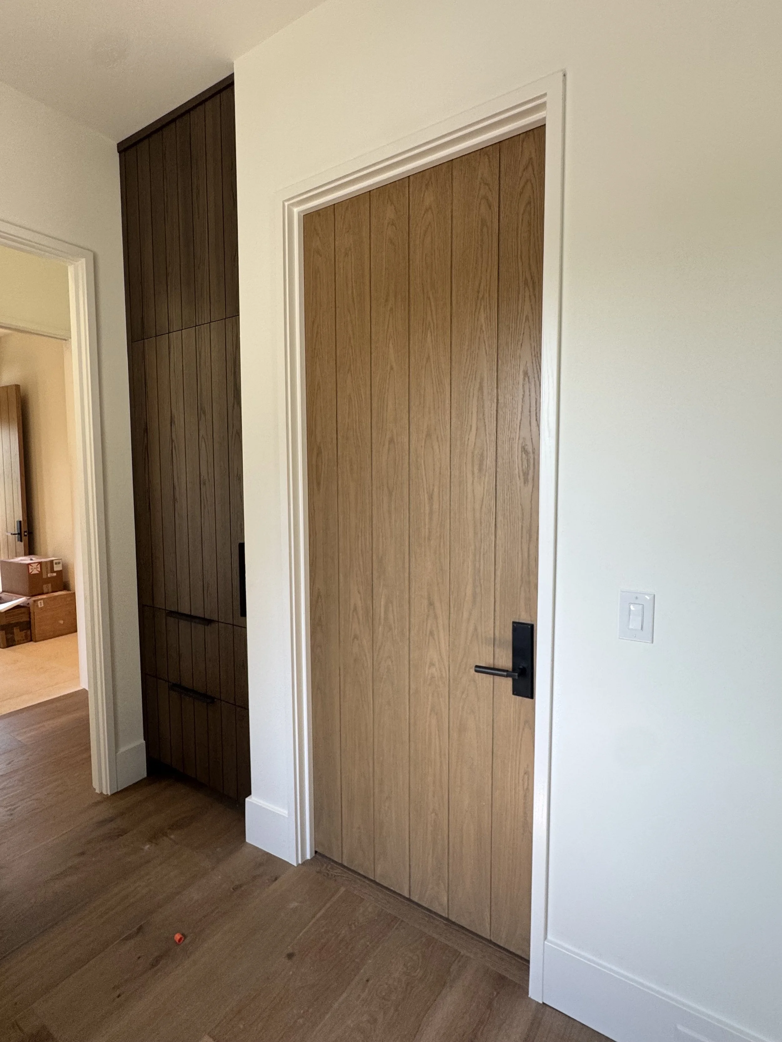 A room with a wooden closet door and a white wall. The floor is wooden, and there are cardboard boxes visible in the background.