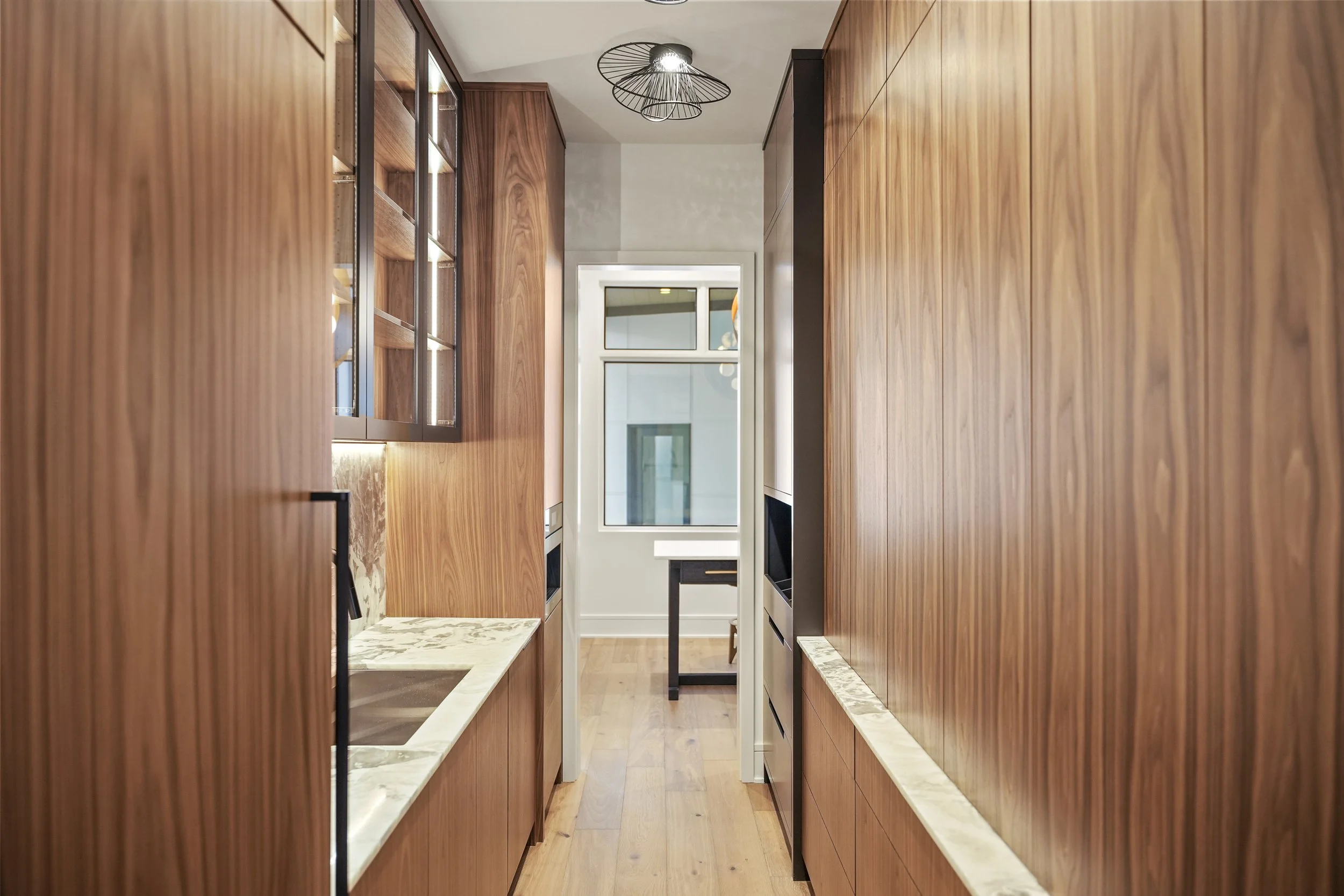 Interior view of a narrow kitchen with wooden cabinets on both sides and a window at the end.
