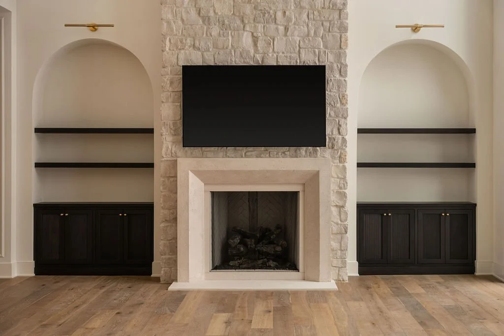 Living room with a stone fireplace, flat-screen TV above the mantel, and built-in shelves on either side with dark cabinets below and open shelves above.