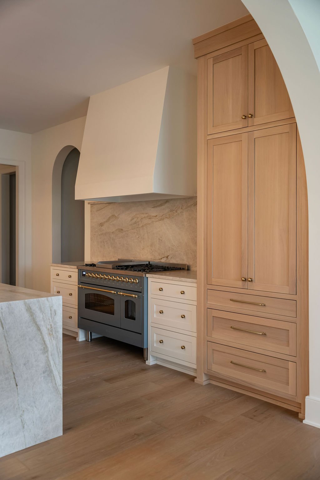 Kitchen with a black stove, white and wooden cabinets, and a marble backsplash and island.