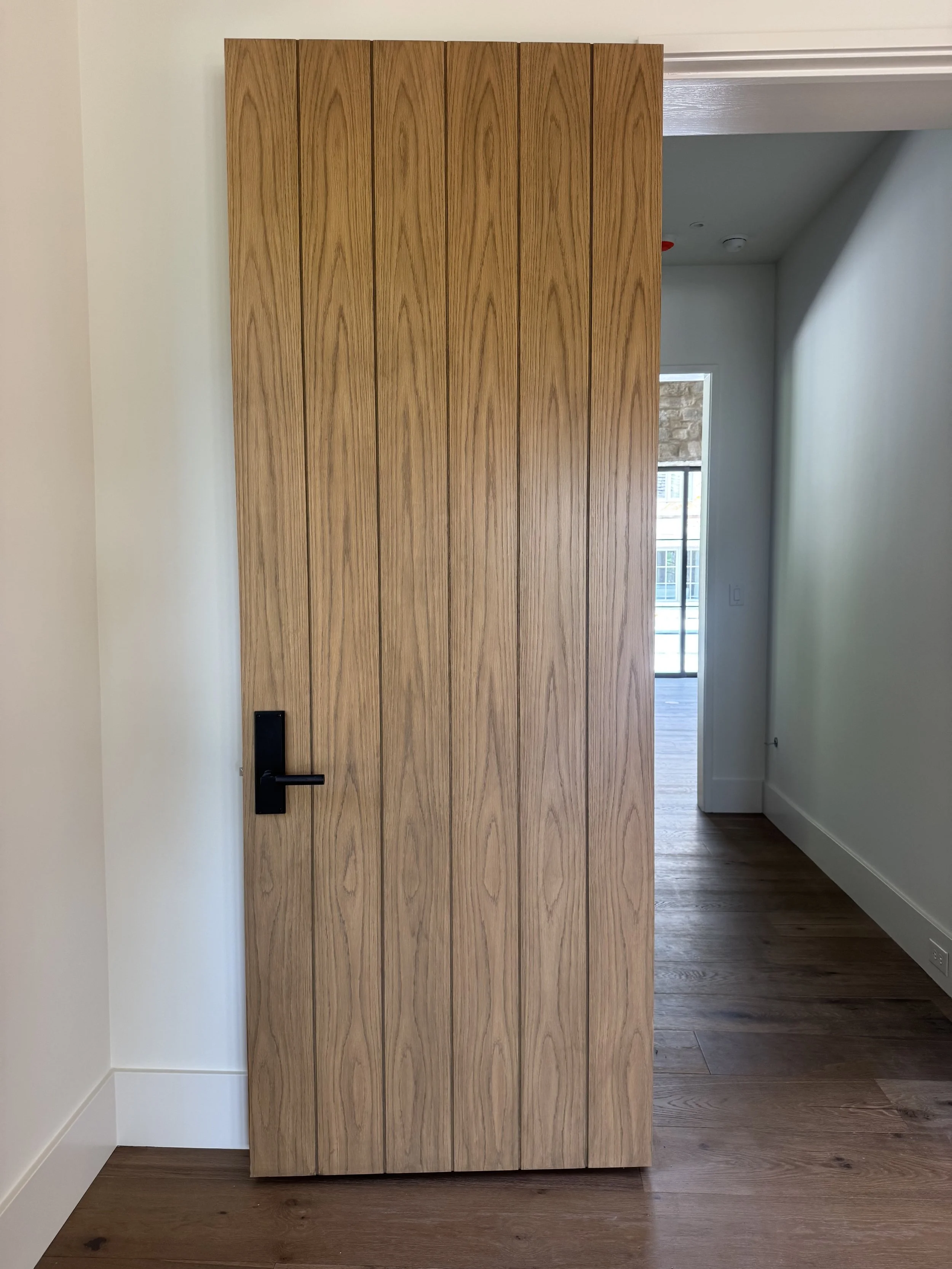 A doorway with a wooden door partially open, revealing a room with a window and wooden flooring.