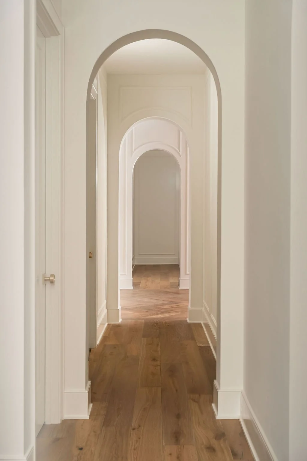 A hallway with arched doorways and wooden floors, painted in neutral tones.