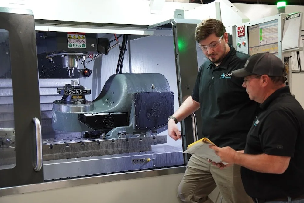 Two workers in black shirts and safety glasses inspecting a CNC machine inside an industrial manufacturing facility. DDM Manufacturing Winston-Salem North Carolina