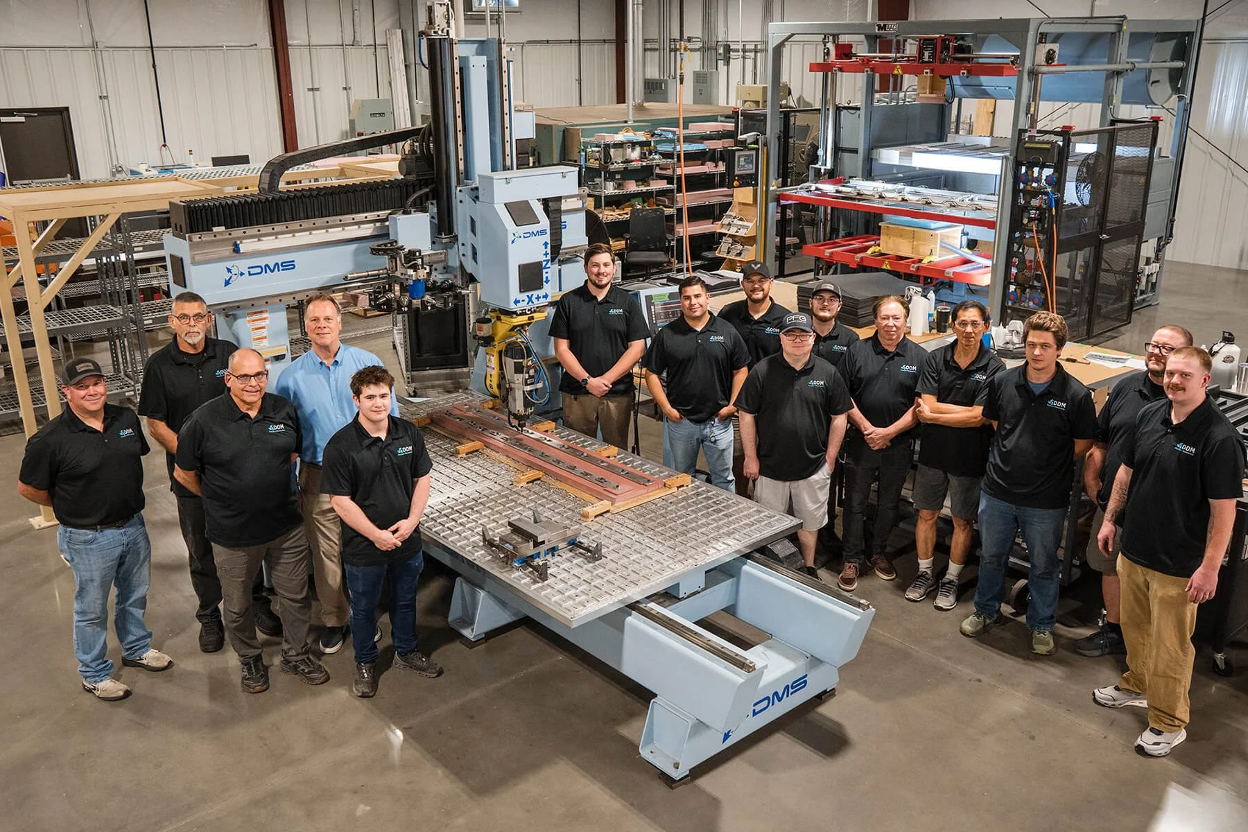A group of people stands together in a manufacturing facility with industrial machines and equipment in the background. low volume high mix machining and forming