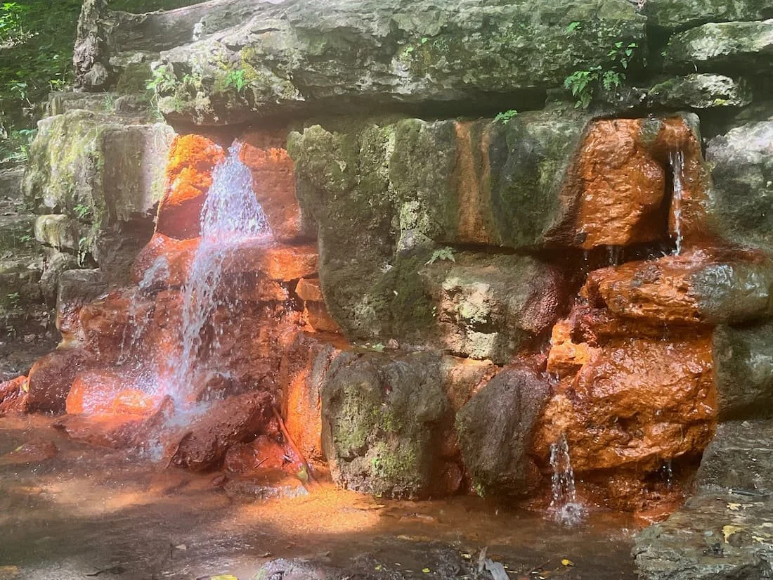 Small waterfall flowing over orange and green moss-covered rocks in a forest setting at Glen Helen Nature Preserve in Yellow Springs, Ohio.