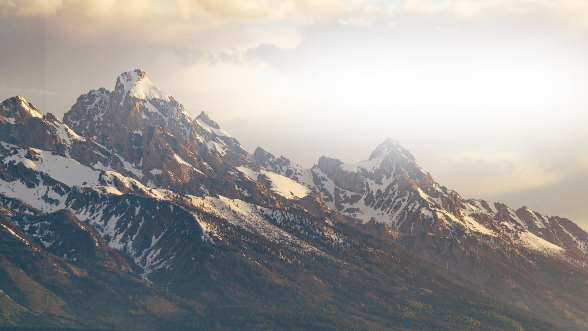 Snow-capped mountain range under a cloudy sky during daytime.