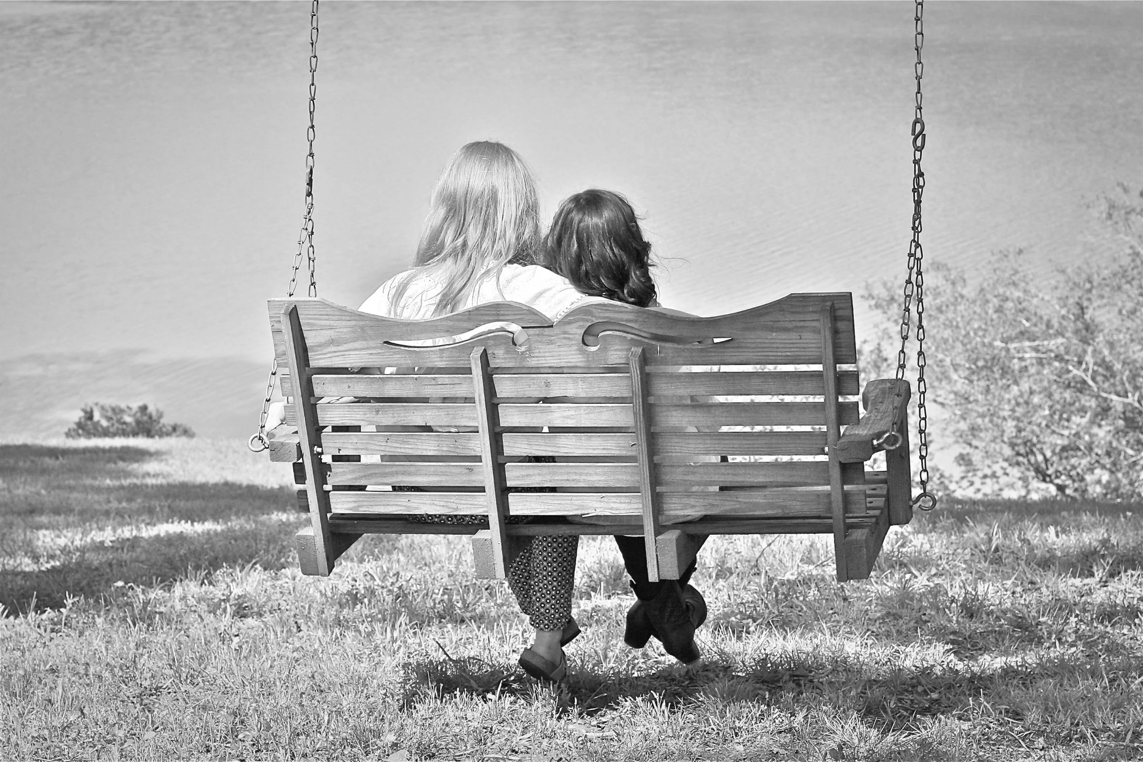A person walking under a child on a swing set in a park, with open sky and grass visible.