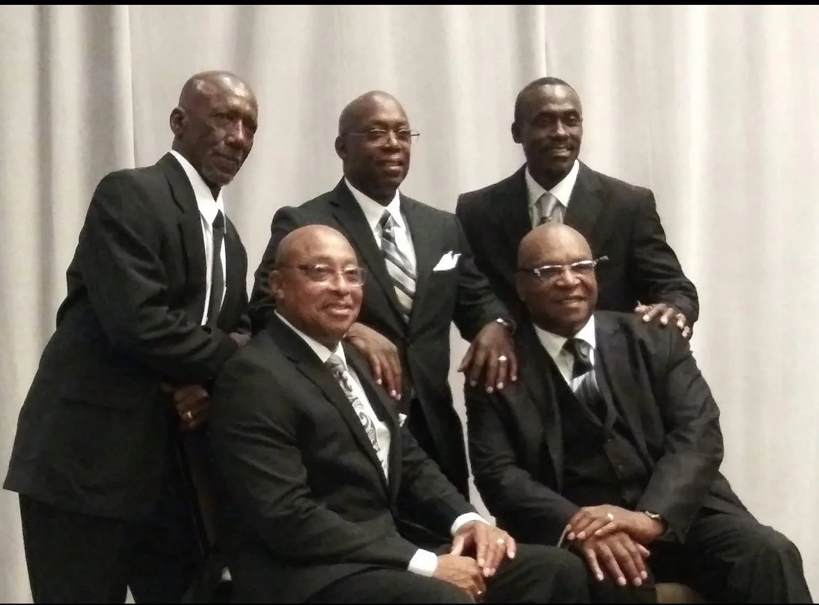 Five men in suits posing for a photo in front of a light curtain.