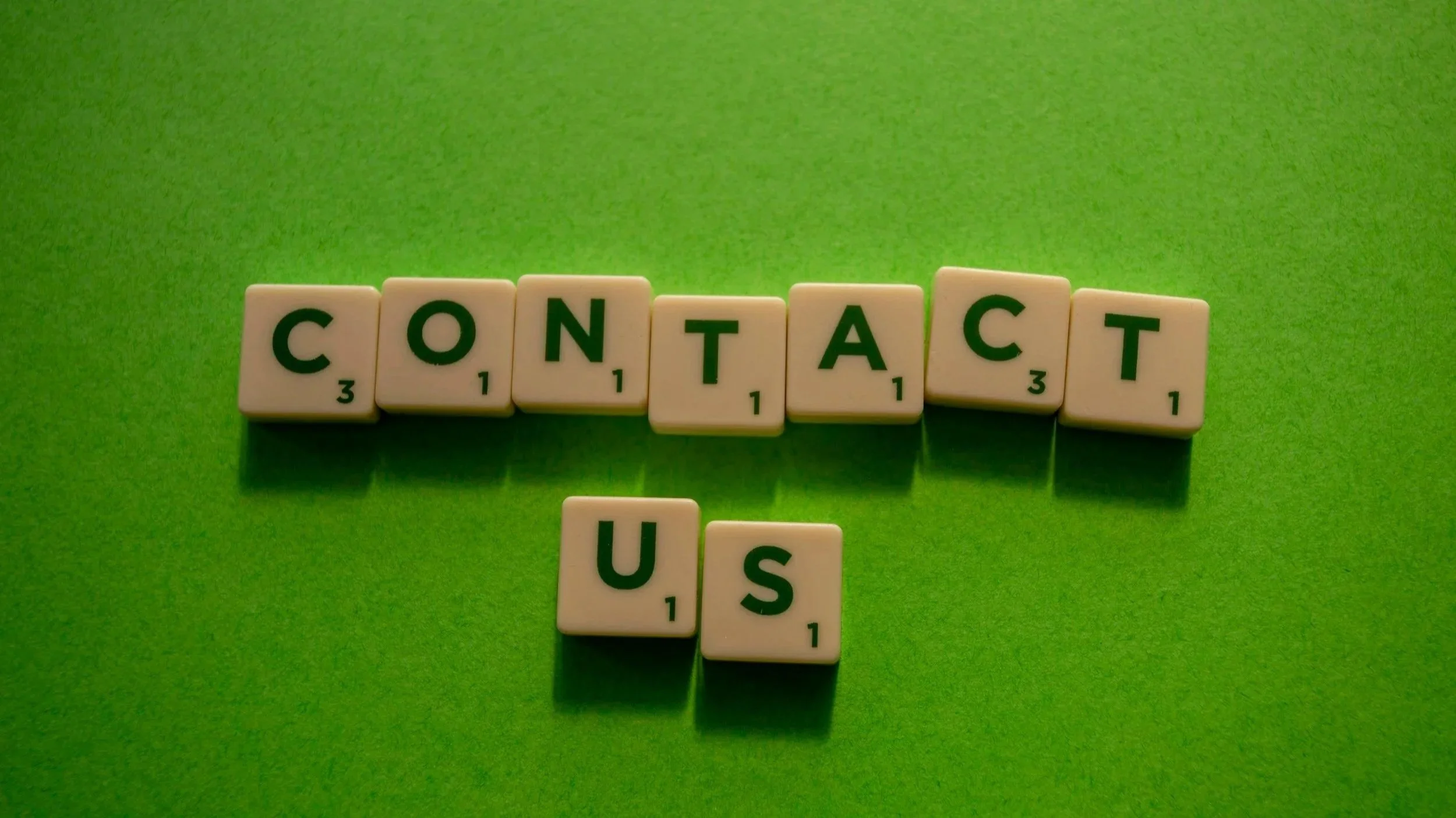 Scrabble tiles spell out 'CONTACT US' on a green background.