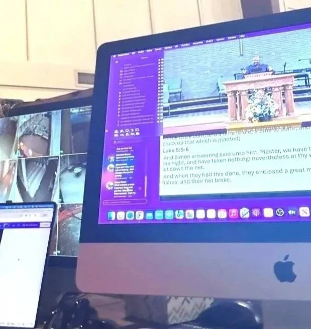 A computer screen displaying a document with text, alongside a sidebar of icons and folders, in a room with other screens and equipment.