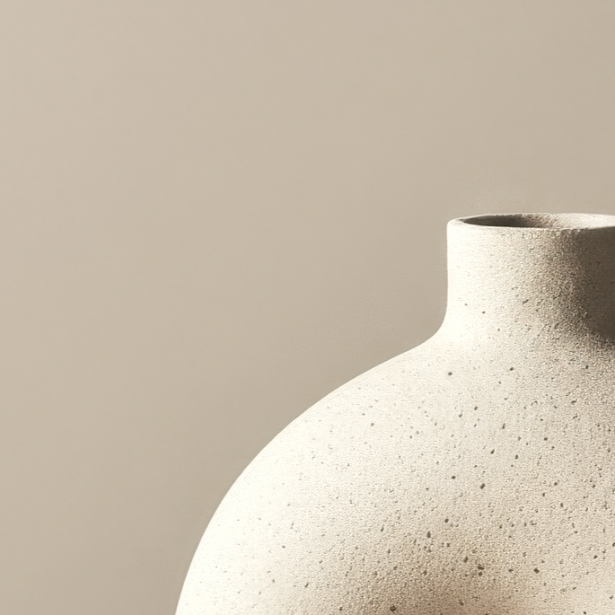 Close-up of a textured, off-white ceramic vase with a rounded body and narrow opening against a neutral background.