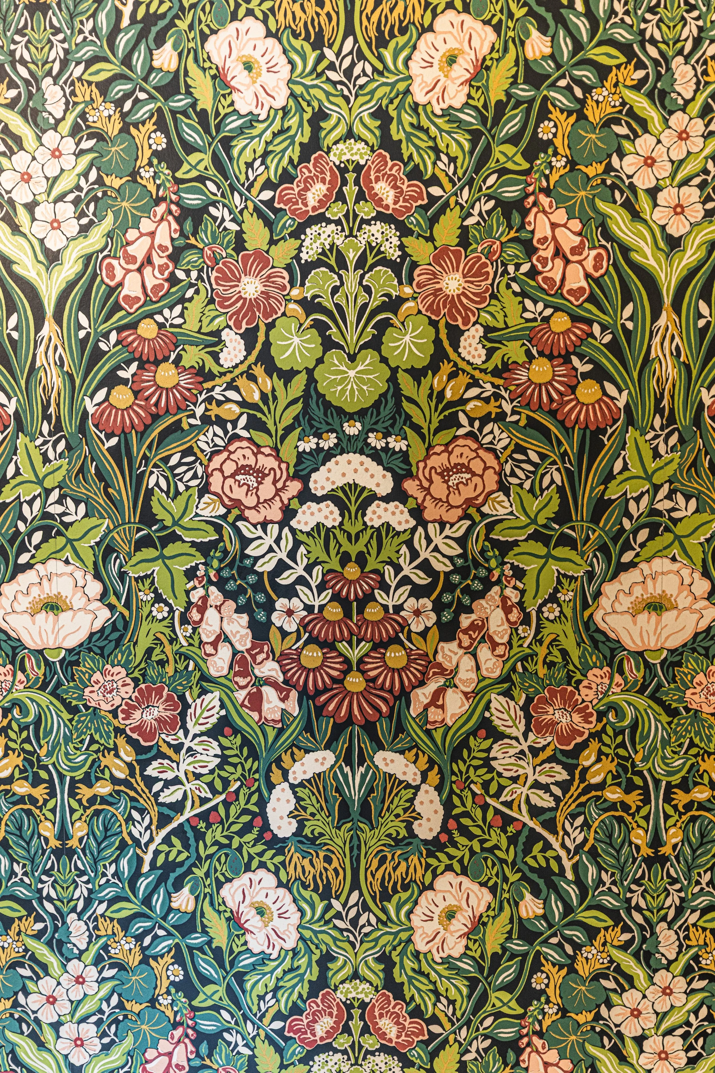 Intricate floral textile pattern with various flowers and green leaves on a black background.