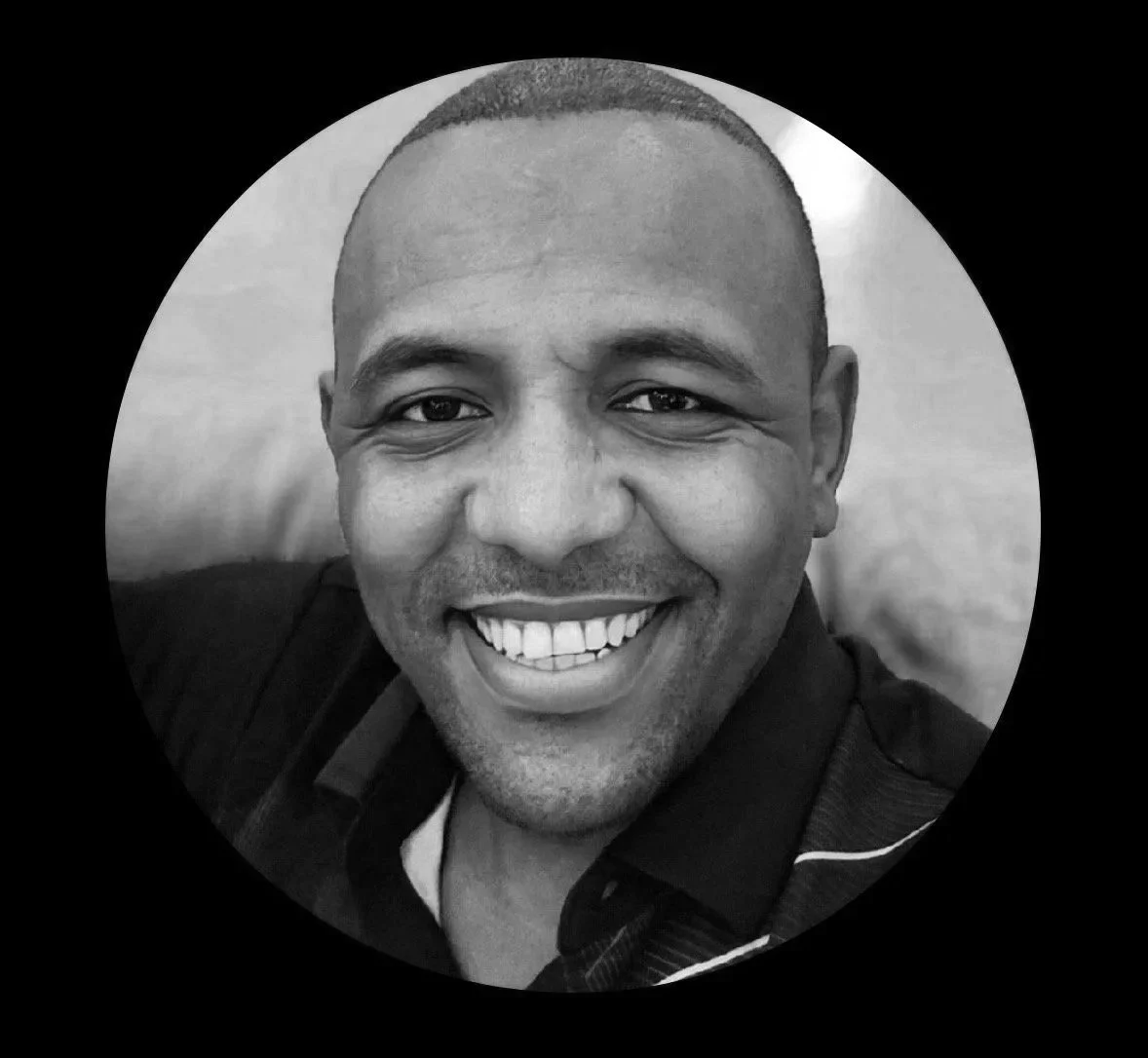 Black and white close-up photo of a smiling man with short hair wearing a dark shirt.