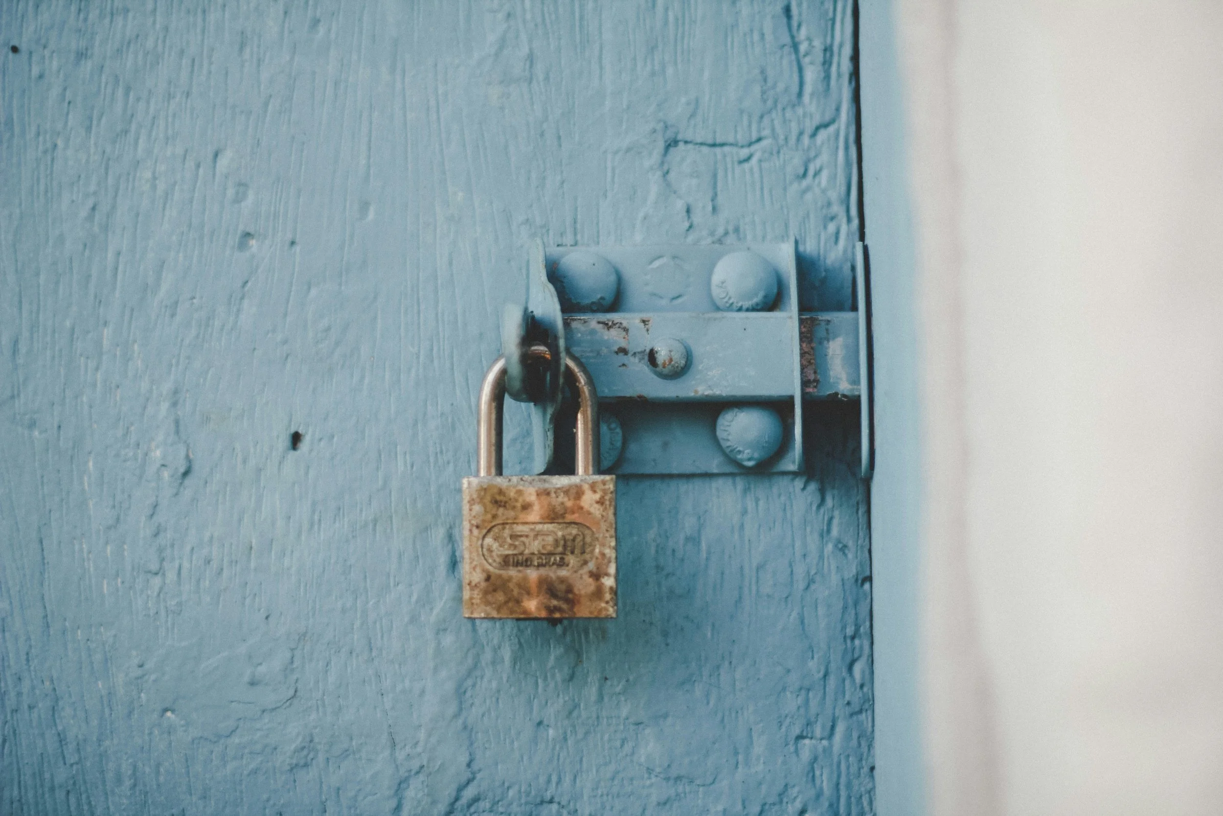private and secure - padlock attached to a blue wooden door with visible grain and imperfections.