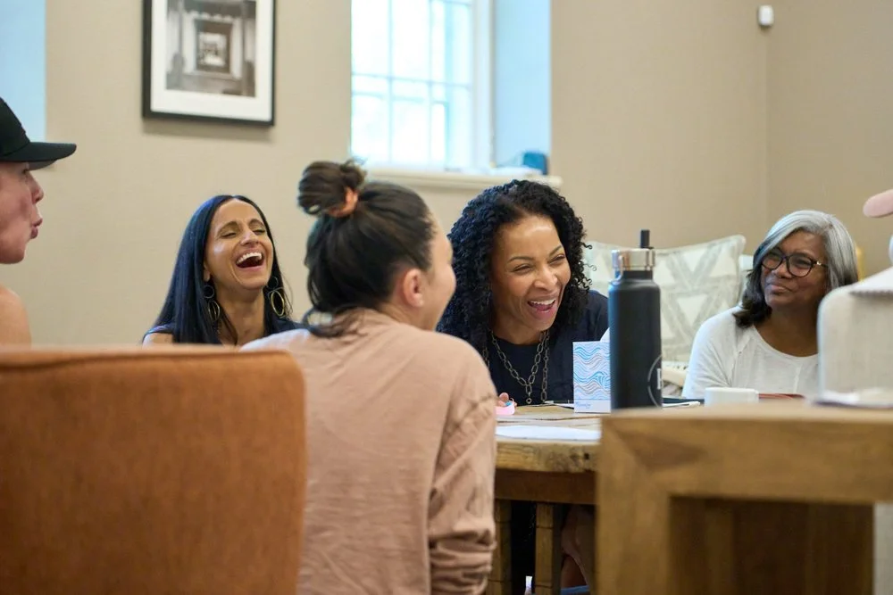 A group of women sitting around a table, laughing and enjoying a conversation at a retreat led by Monisha Chandanani.