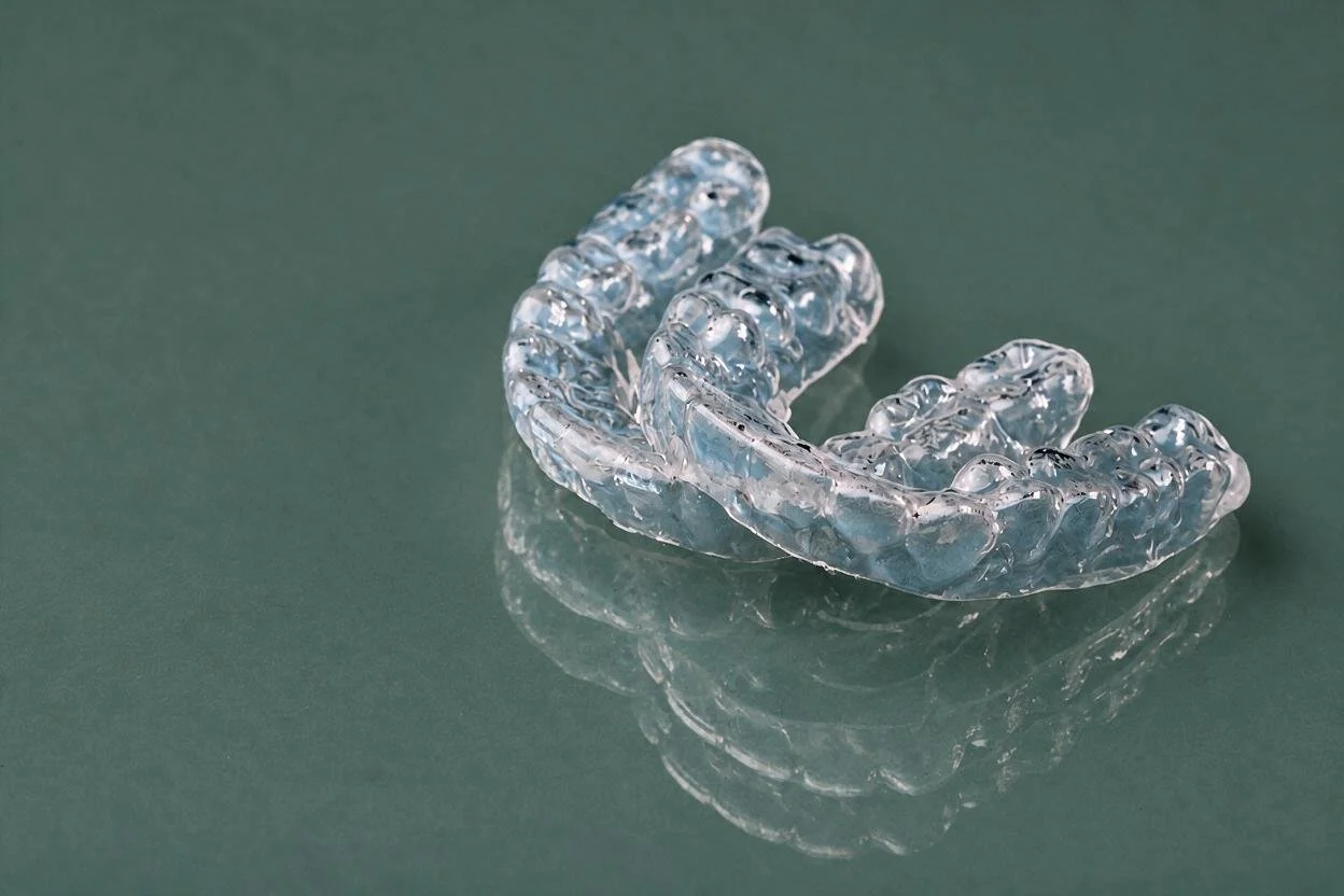 A pair of clear aligner trays resting on a reflective green surface, representing discreet orthodontic treatment options at Gil Orthodontics in Dripping Springs.