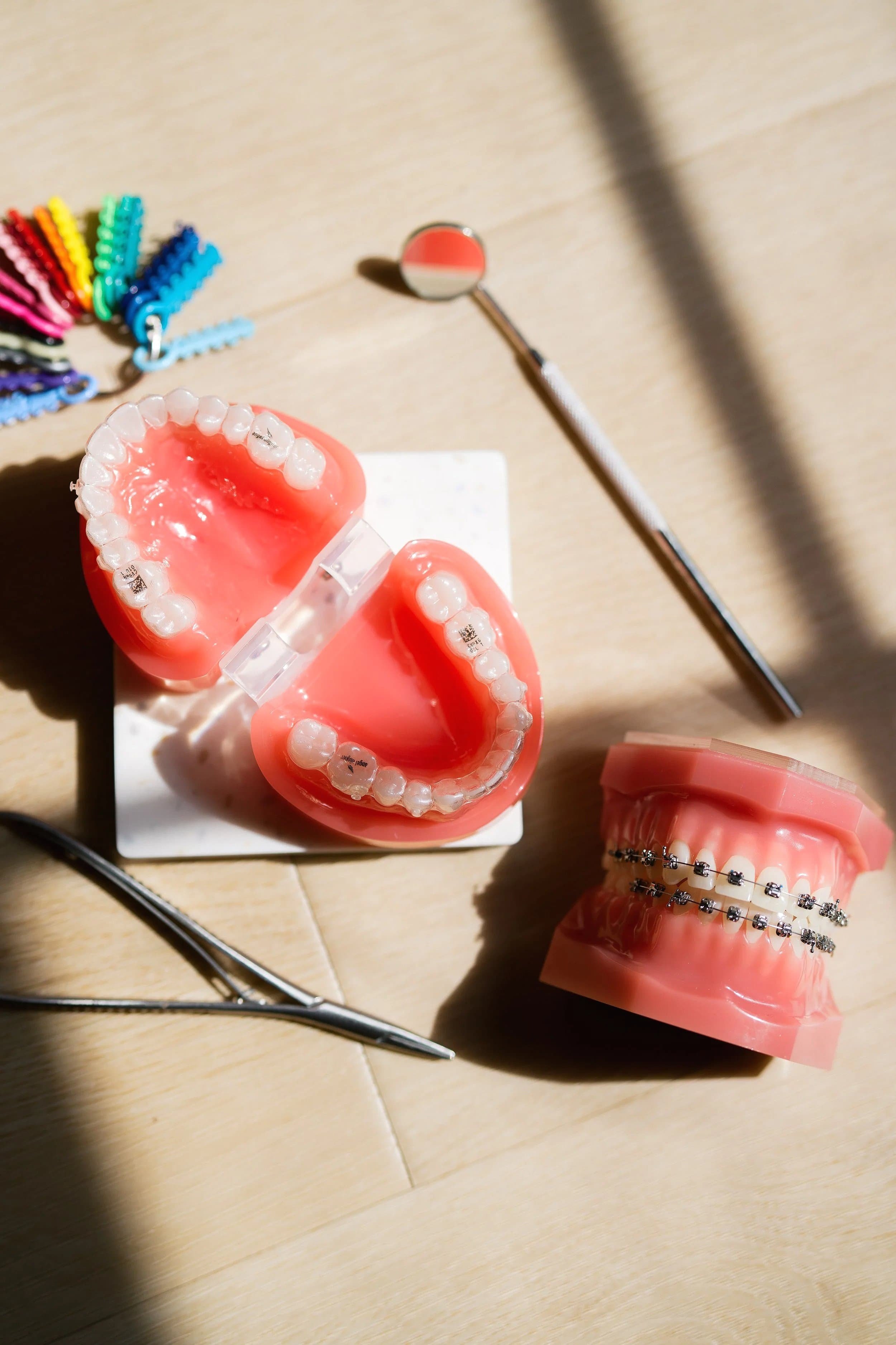 Dental models displaying clear aligner trays and traditional metal braces alongside colorful elastics and a dental mirror, representing the variety of orthodontic treatment options at Gil Orthodontics in Dripping Springs.