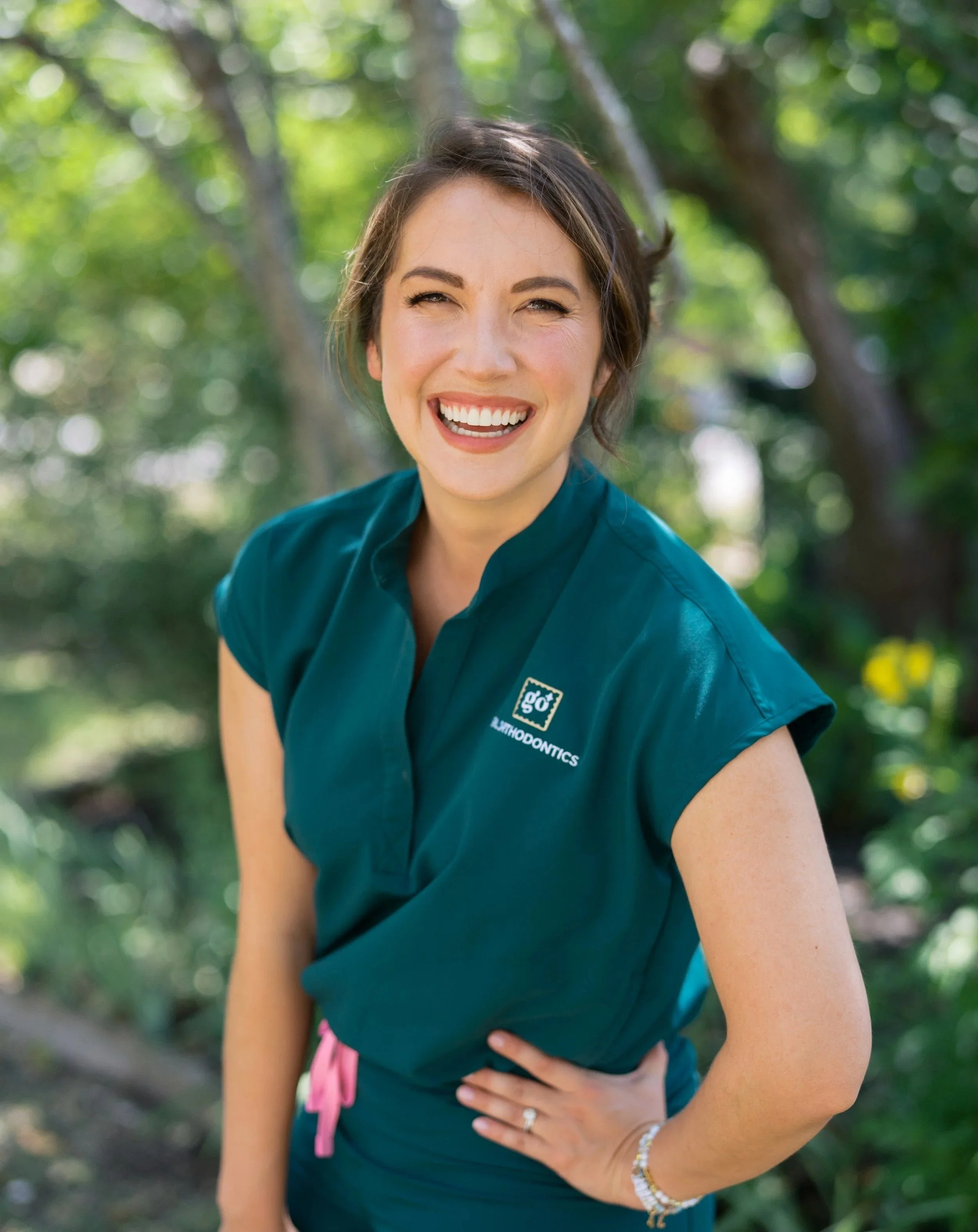 Dr. Avery Gil smiling outdoors wearing a green Gil Orthodontics shirt in Dripping Springs, Texas.