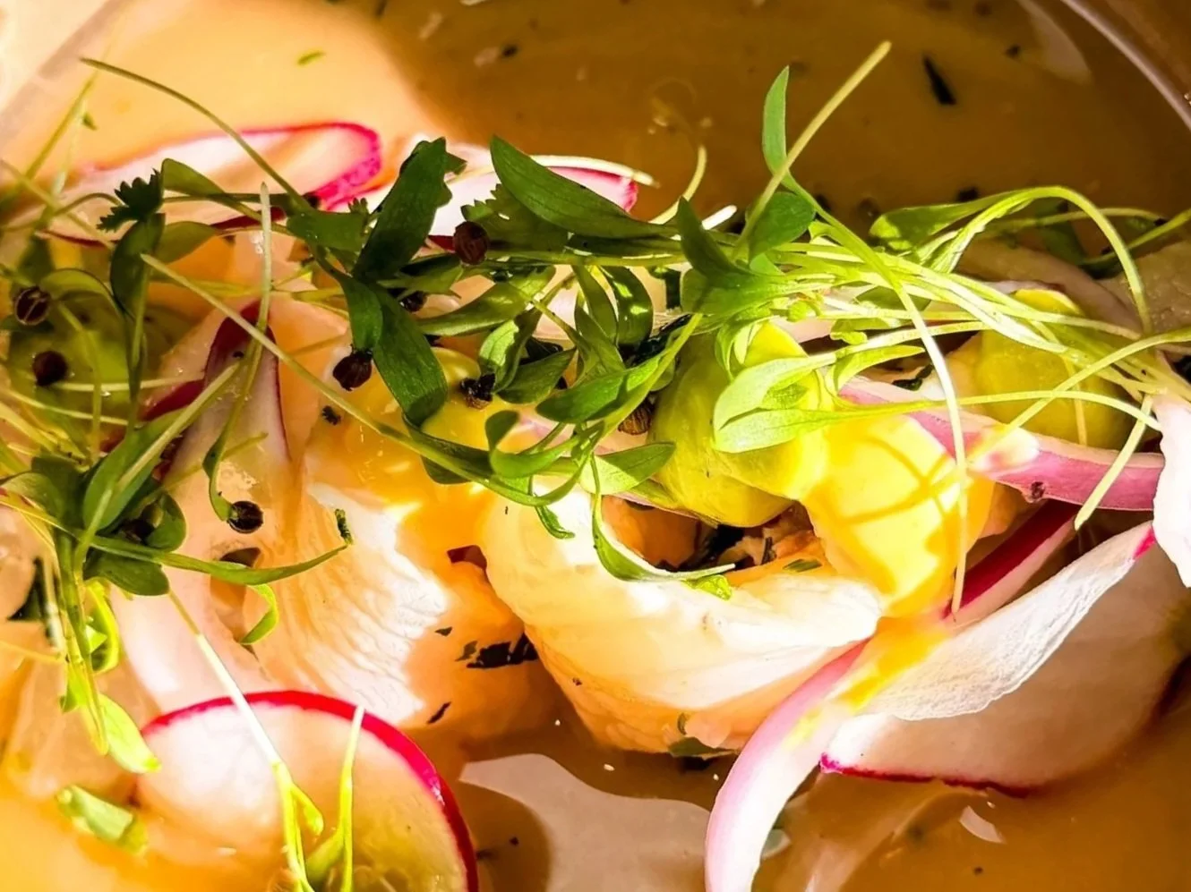 Close-up of a dish with sliced radishes, microgreens, and a poached egg in a yellow sauce.