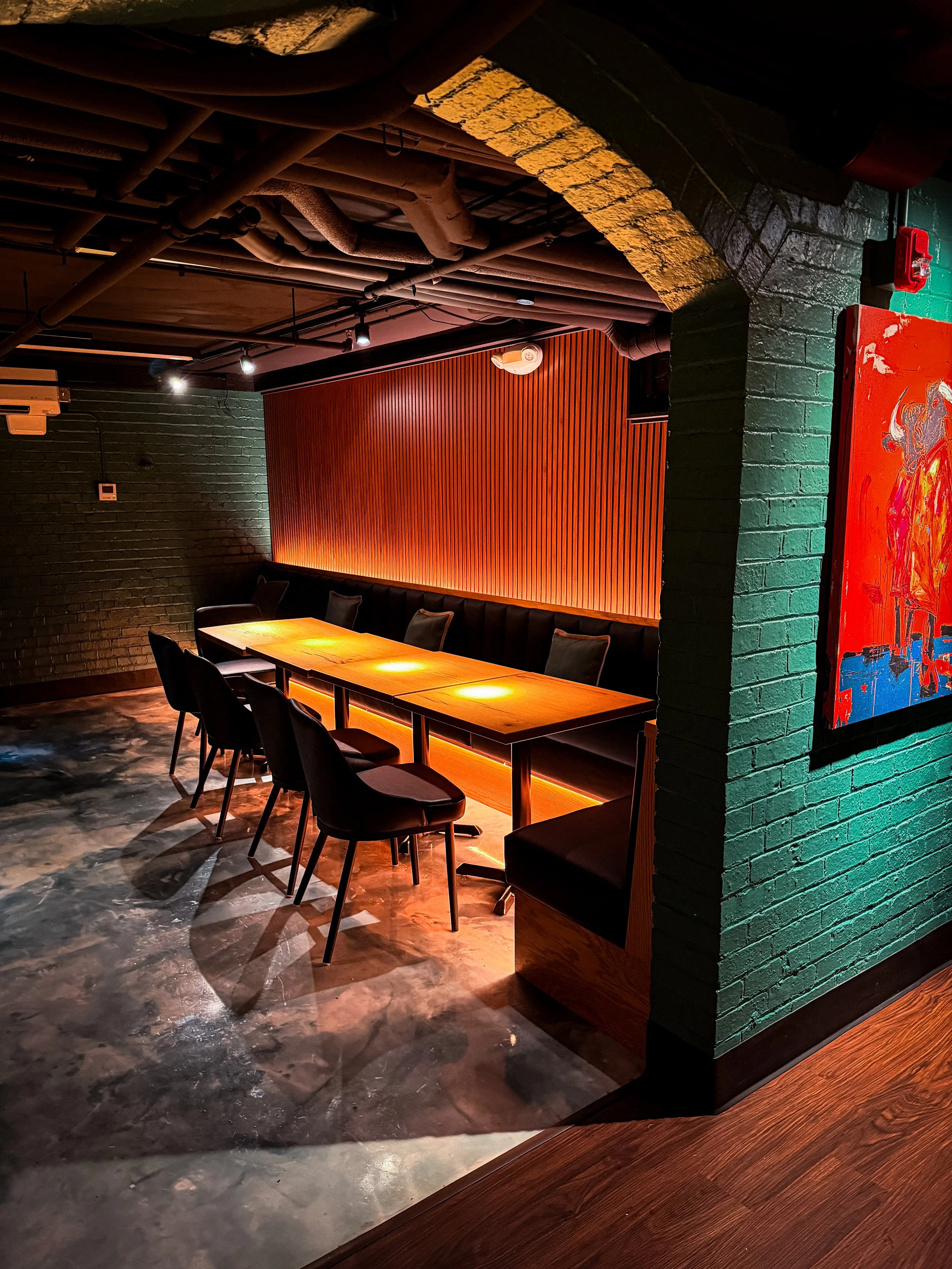 A dimly lit restaurant or bar with a long wooden table and black chairs. 