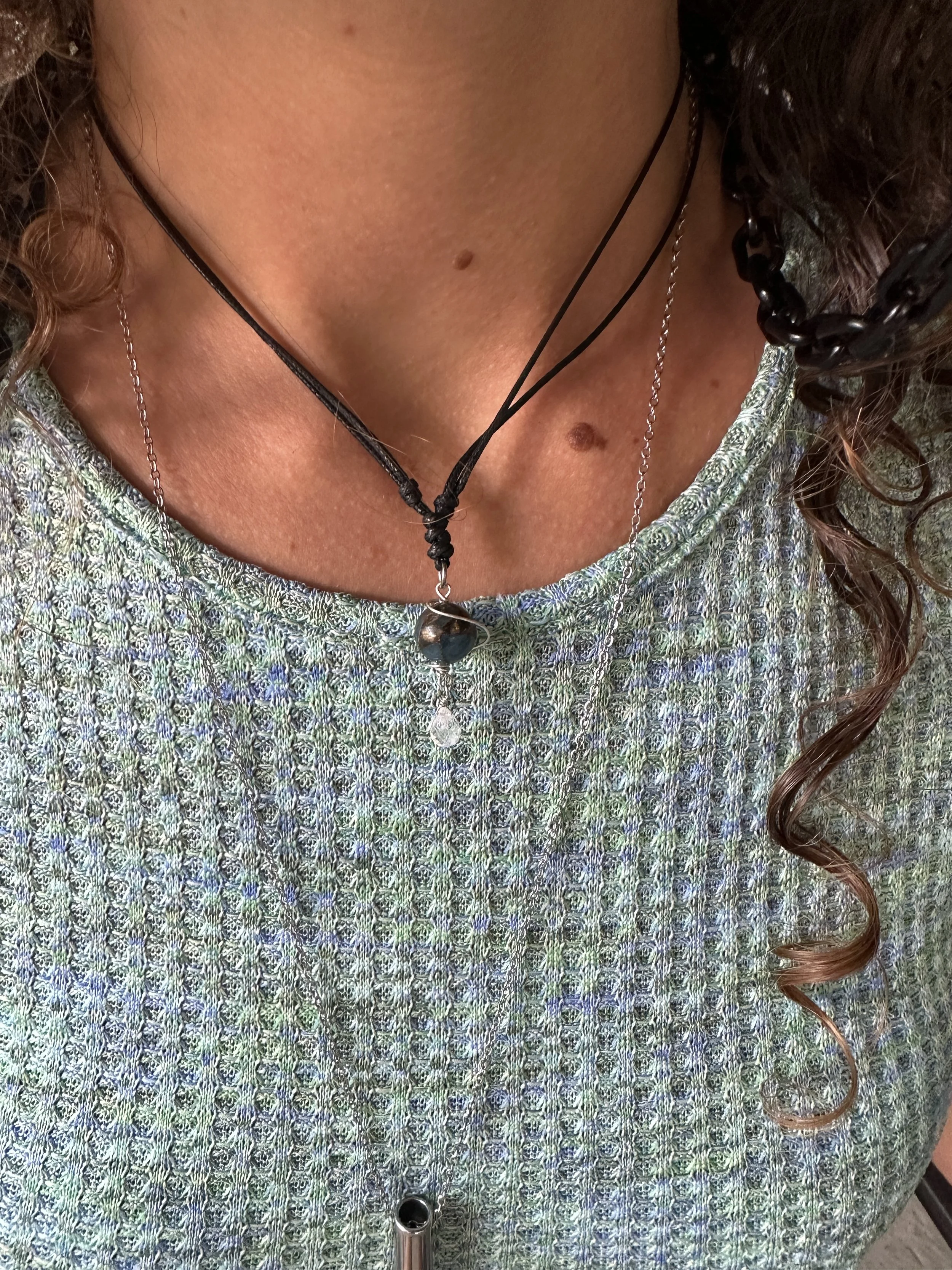Close-up of a woman's chest and part of her face, showing her wearing layered necklaces and a patterned top.