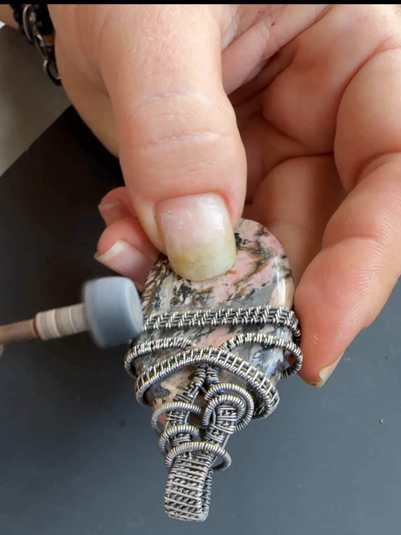 Close-up of a person’s hand with jewelry and rings, holding a polished stone pendant attached to a silver chain.
