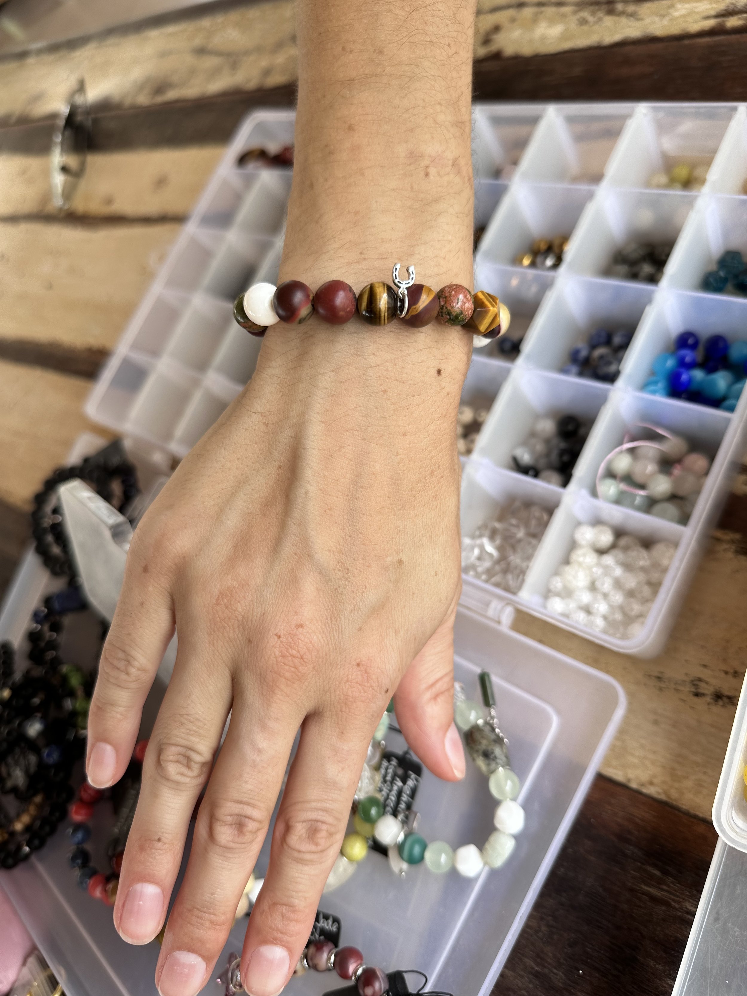 Hands displaying jewelry on fingers and wrists with storage containers of beads in the background.